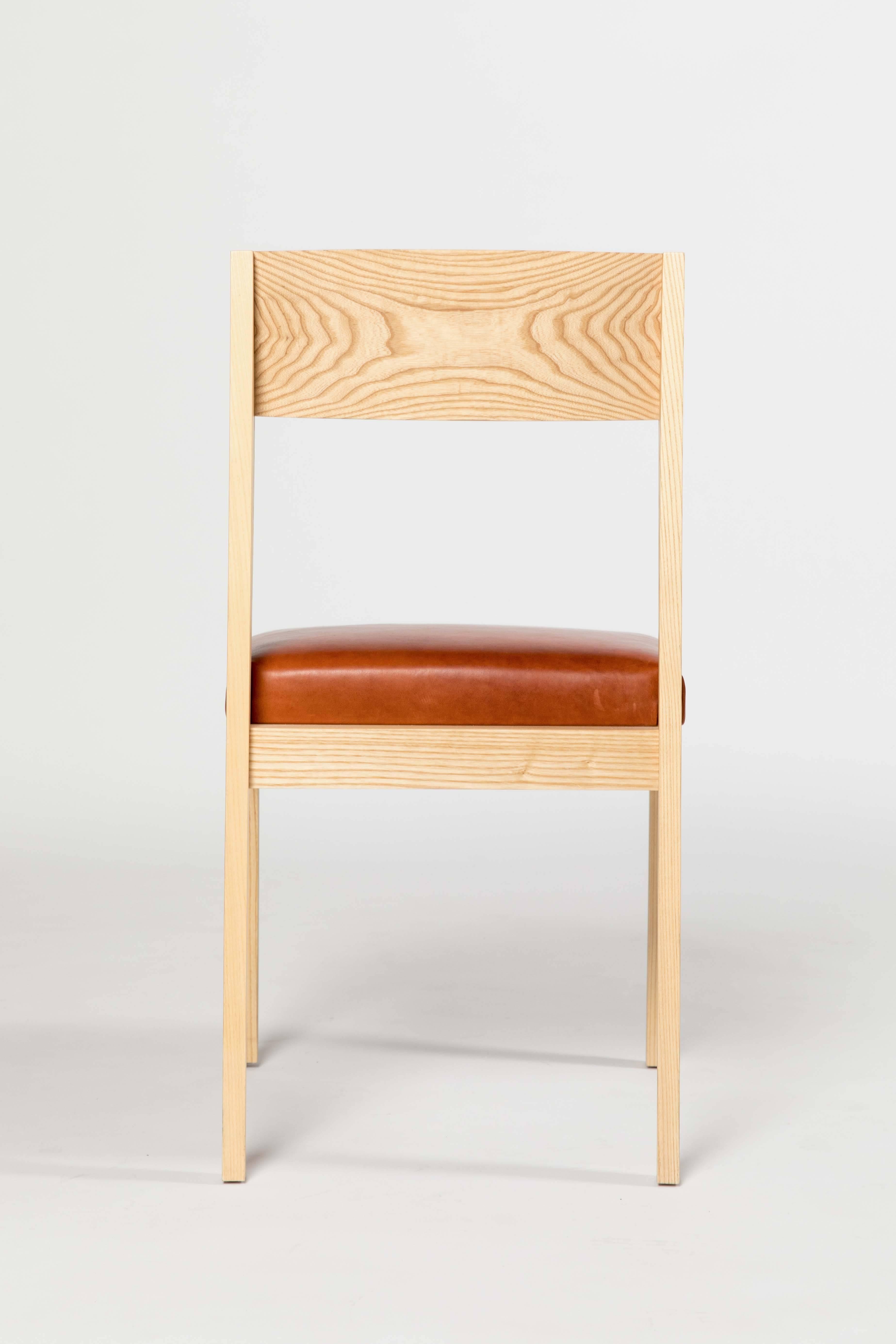 The Shelley chair by Kate Duncan is handcrafted from solid wood. It incorporates clean lines and intersecting angles to maximize comfort. This dining chair features a sloped curved back that cradles resting shoulders and a leather seat with