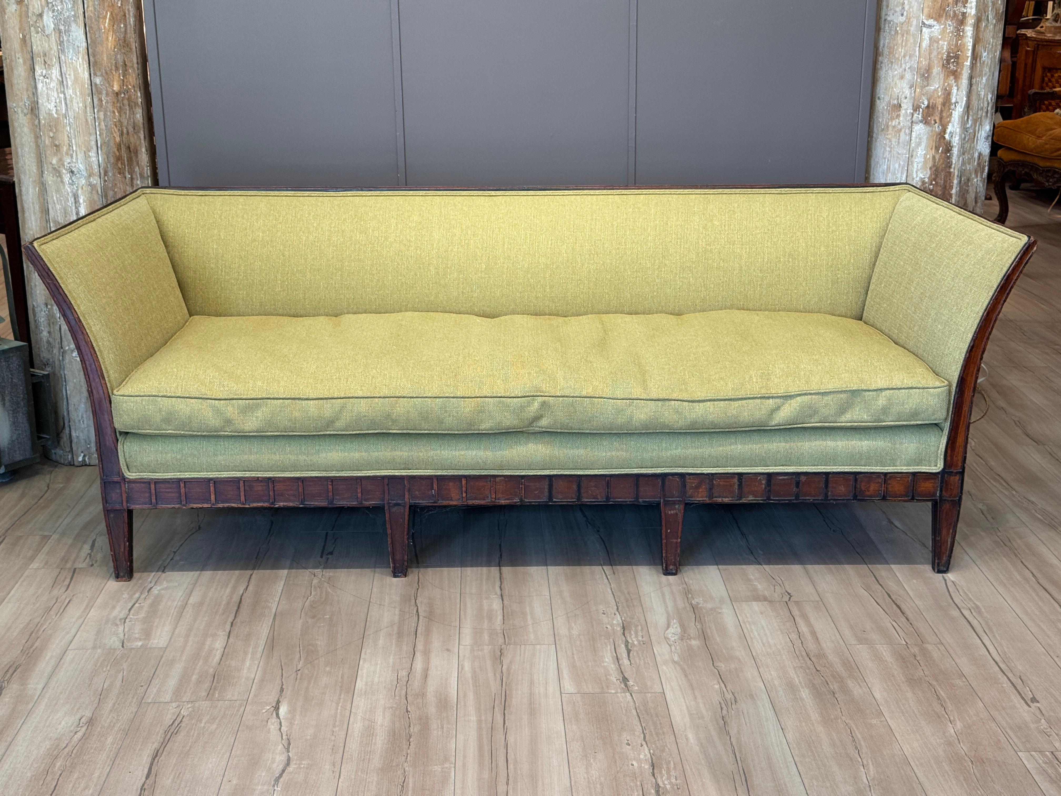 Elegante sofá italiano de principios del siglo XIX, con armazón de nogal tallado y laterales suavemente abocinados. La estructura presenta detalles verticales en forma de lengüeta a lo largo del faldón y las patas, que soportan un respaldo y un
