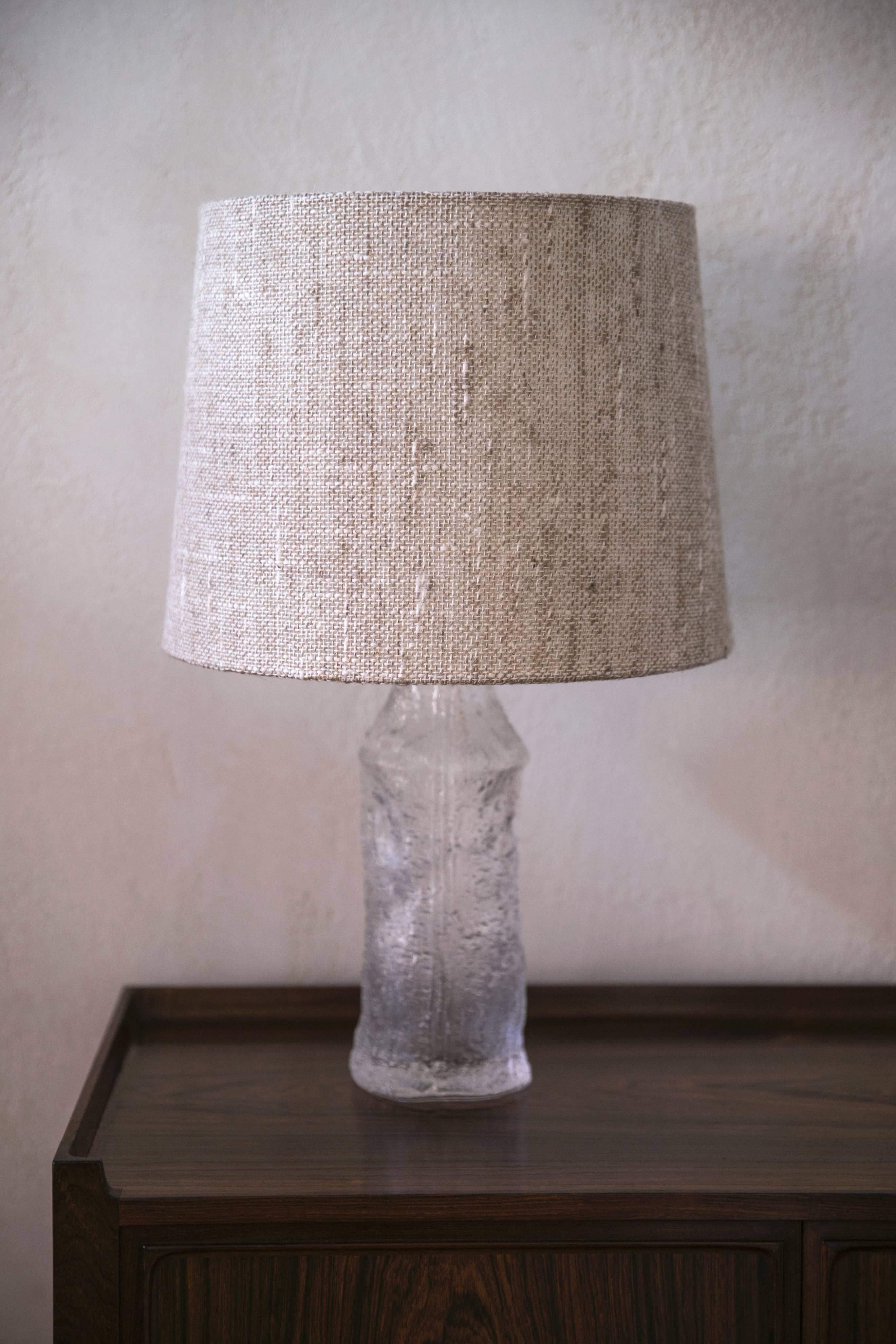 These molded glass lamps in tree trunk form retain their original period linen shades. Made circa 1964 for Iittala, Finland by Luxus of Sweden.

Overall height 20 inches.
Glass base height 10 5/8 inches.
Glass base diameter 4 1/8 inches.
Shade