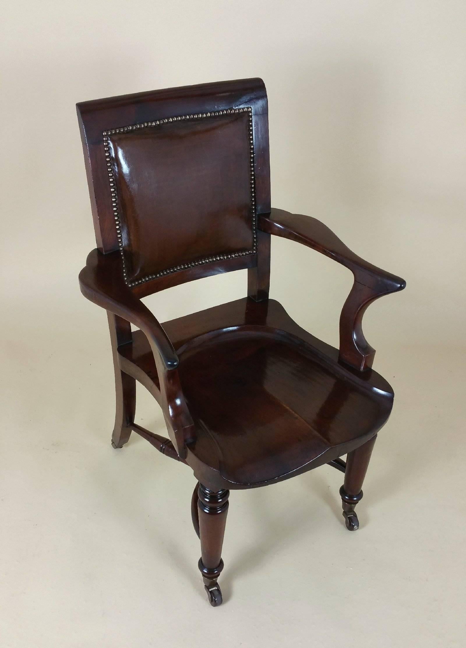 This gorgeous and superb quality Victorian mahogany desk chair features a solid, carved and shaped seat with an upholstered leather inset on the back and brass stud trim. The chair features swept back and turned front legs, all on brown ceramic