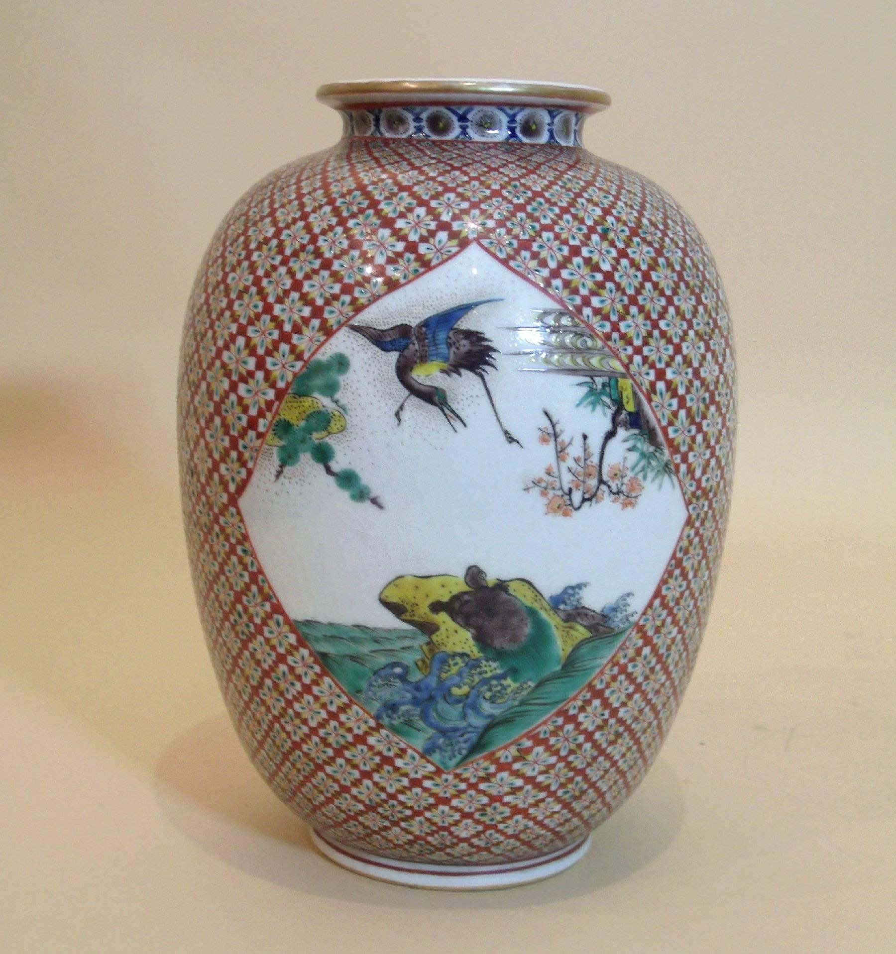 This exquisite Japanese Ko-Kutani amphora shaped pottery vase features a delicate and intricate design surrounding a scenic image on either side. The dark red, green, yellow and white color scheme makes up a striking petal-like pattern.  The vase is