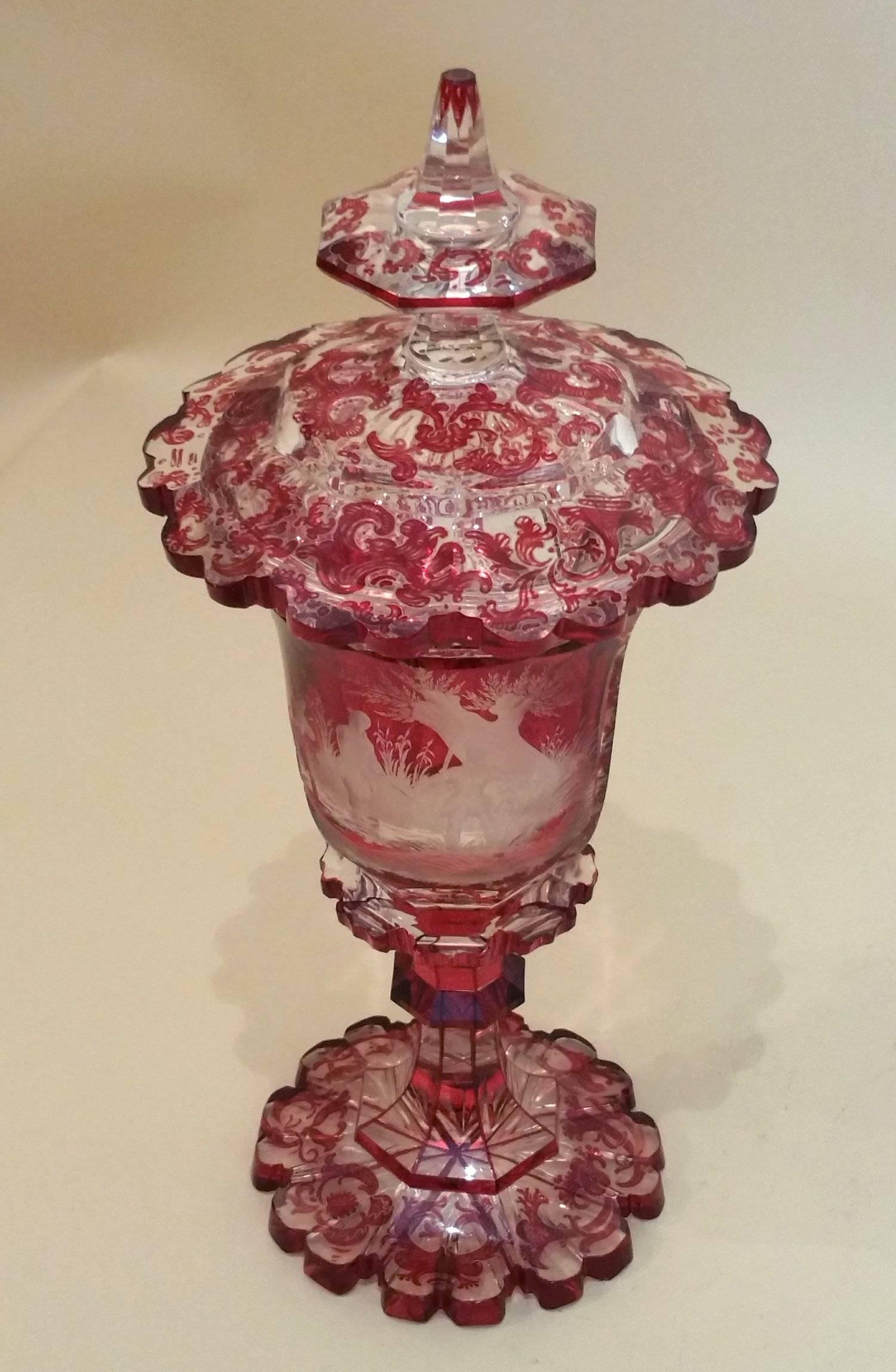 This superb 19th century Bohemian ruby overlaid glass vase and cover features a magnificent and intricate all-over design. The central area of the vase depicts an engraved hunting scene, with a clear oval ‘window’ on the opposite side so the