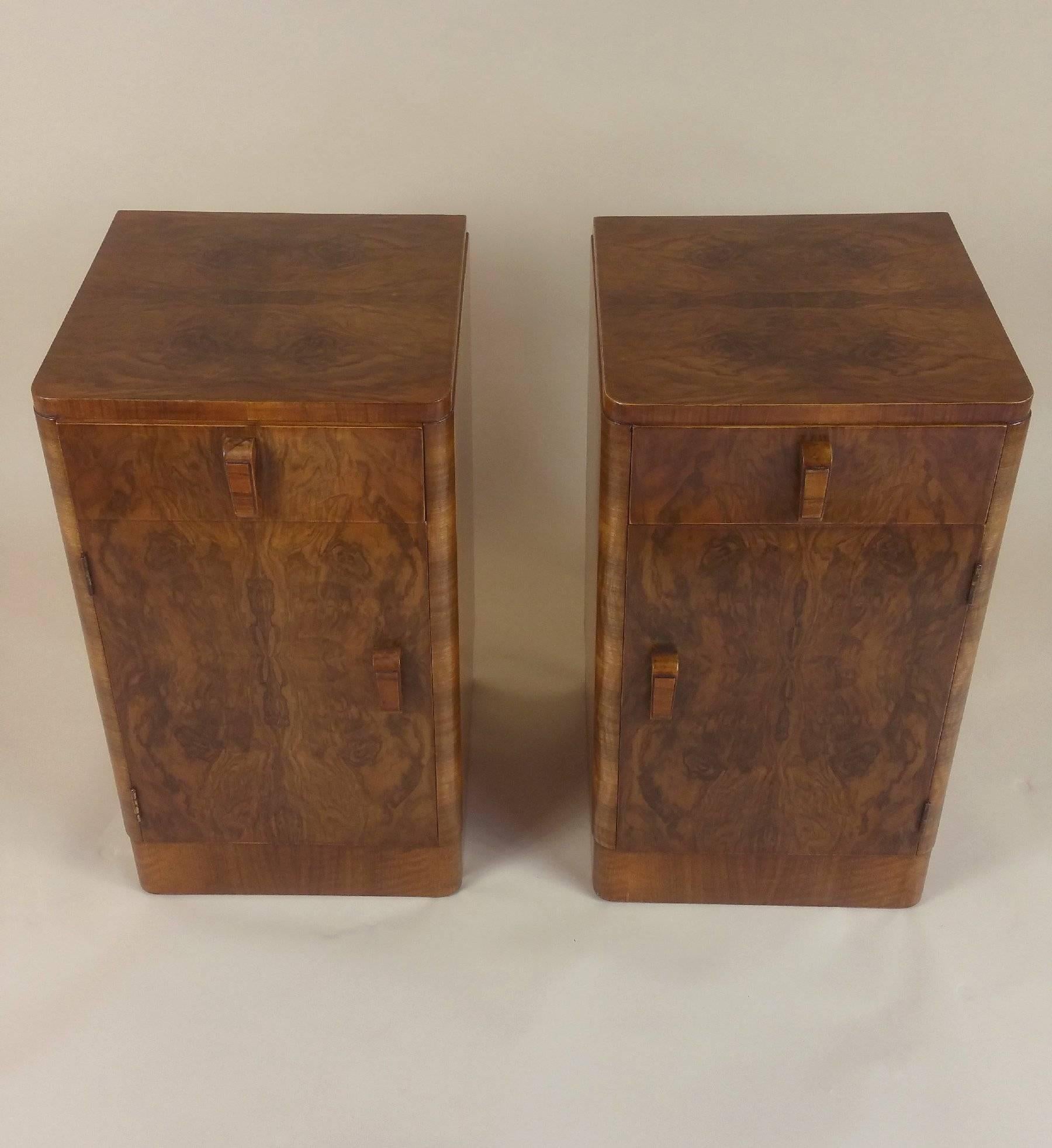 This handsome pair of figured walnut Art Deco bedside cupboards feature a top drawer over a cupboard door that opens to a central dividing shelf. They have Classic Art Deco design and detailing with shaped wood drawer and door pulls. Each cupboard