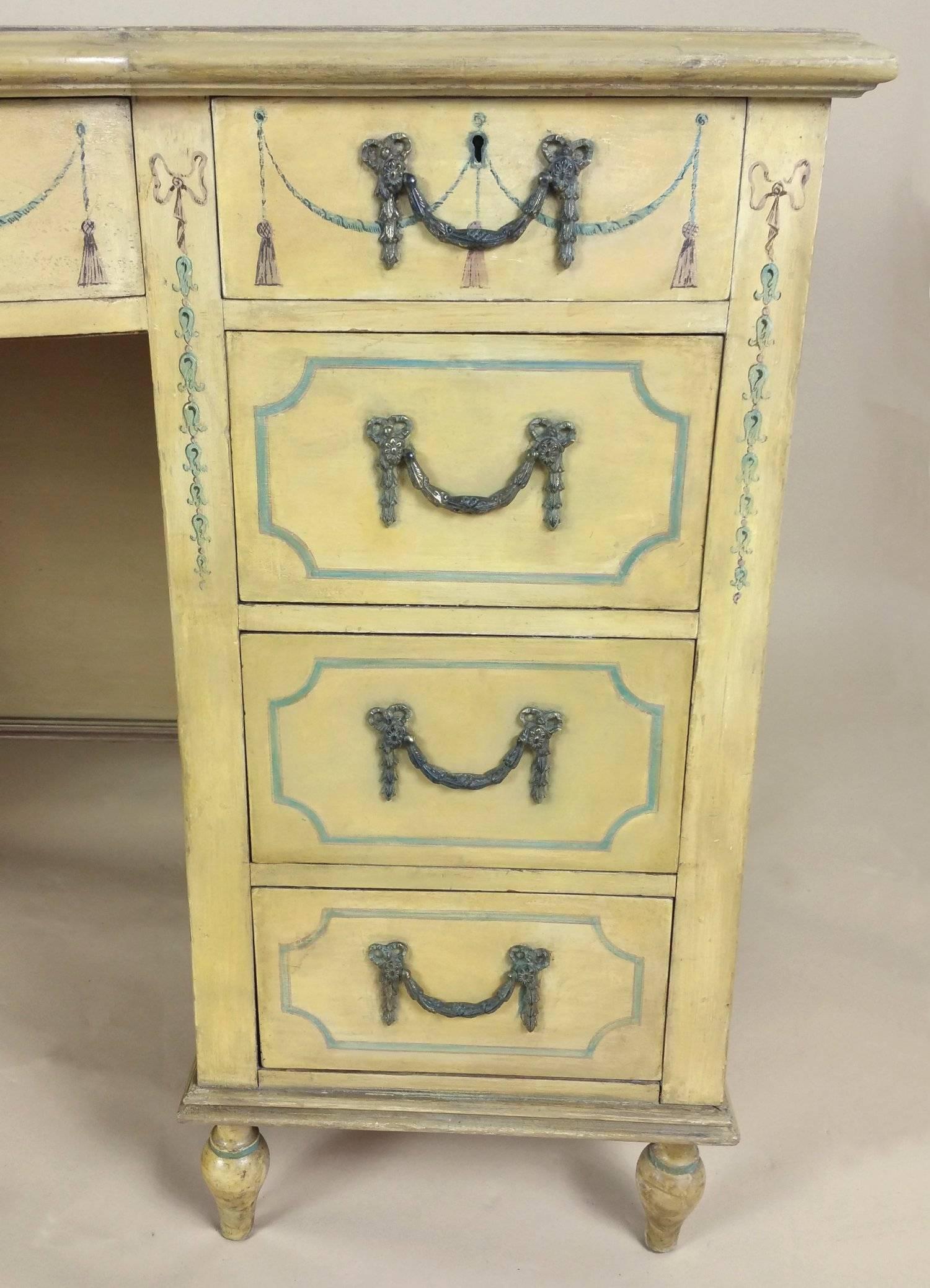 This unusually styled Edwardian cream painted knee hole desk features curved, shaped sides and a bow center front on six turned supports. The desk has one central top drawer flanked with four drawers on either side, with detailed swag and bow styled