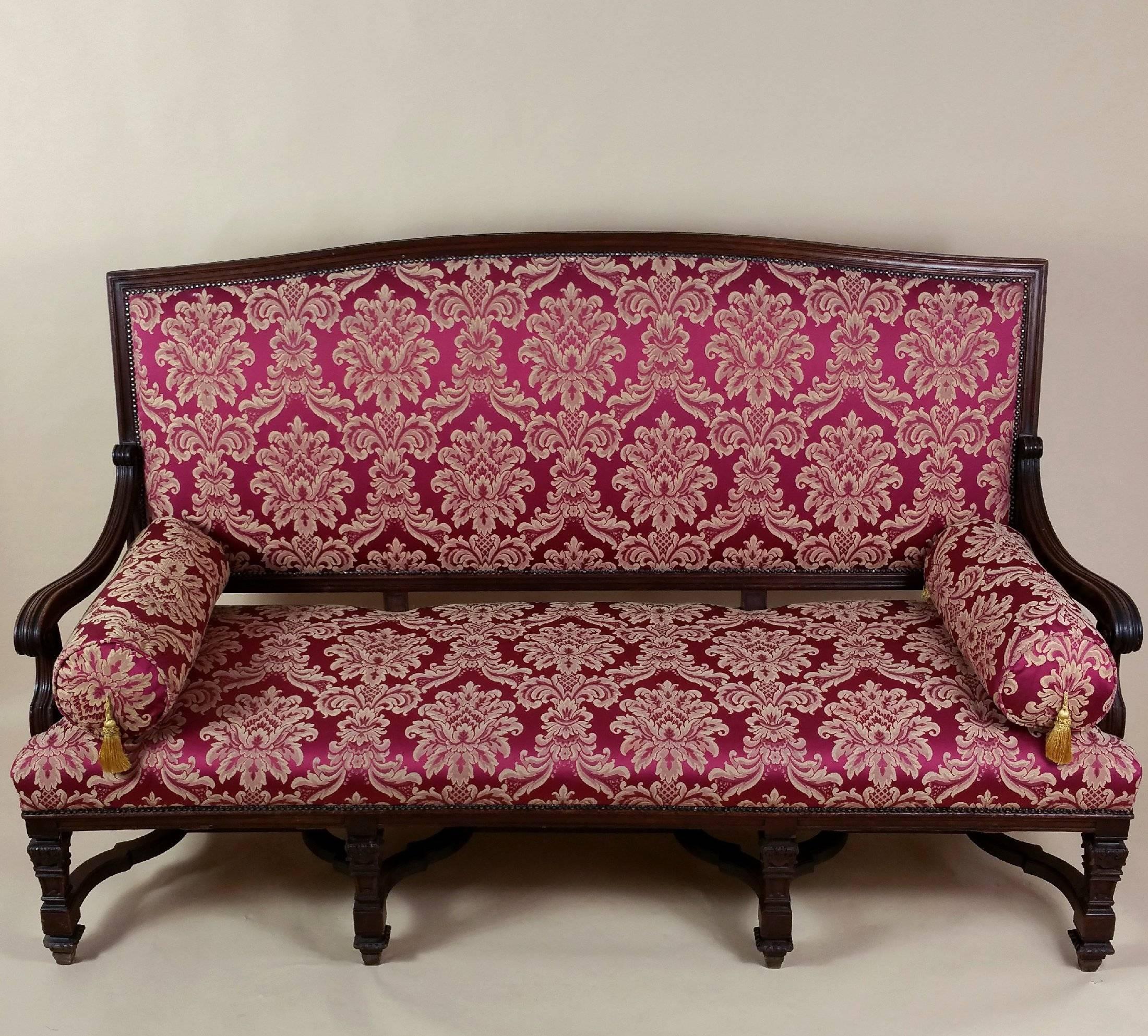 This magnificent and beautifully crafted Victorian couch features carved walnut frame with acanthus leaf detail and a decoratively shaped stretcher base. The couch is upholstered in a dark burgundy and cream silk damask fabric with a separate rolled