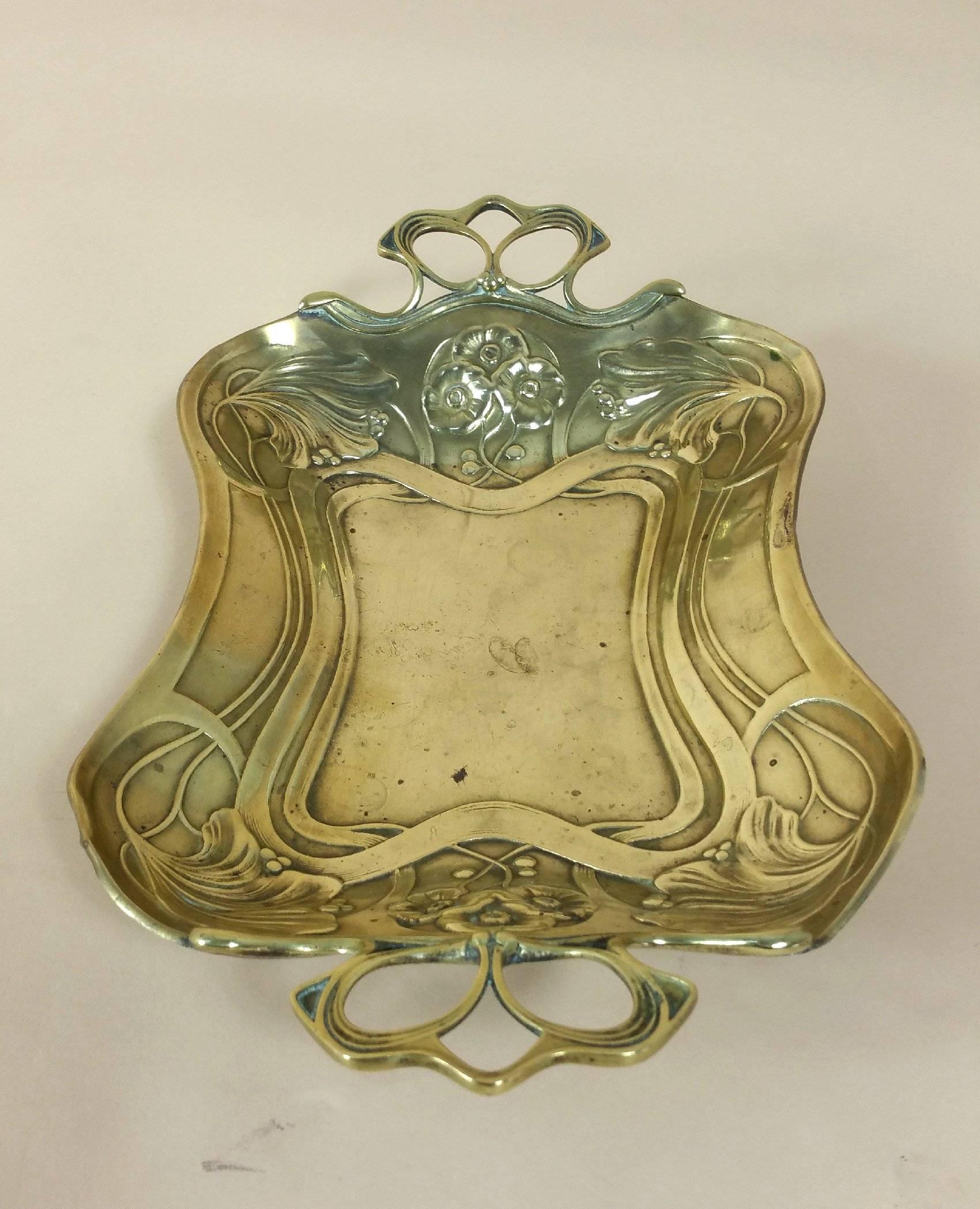 This highly decorative Art Nouveau twin handled brass dish is decorated with stylized flowers and stamped C.L.D. The top side of the dish is in very good condition and with the odd mark or blemish. The back has several more marks and worn areas, but