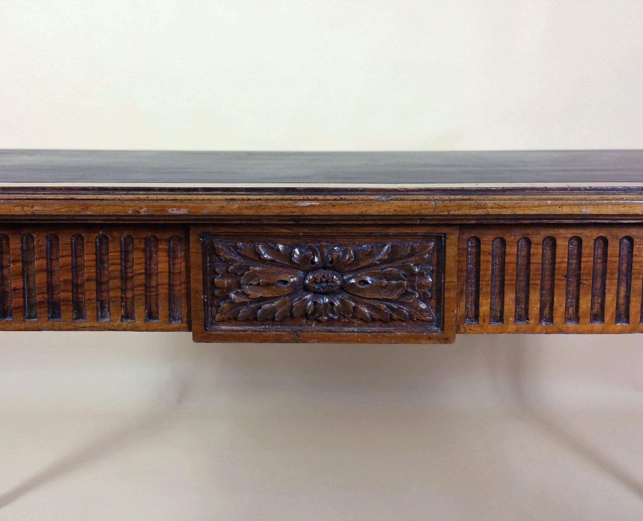 This gorgeous and classic Victorian walnut library table features a wonderfully carved design around the apron and turned tapered legs. The table has a drawer on each end and retains the original leather top. It also has a makers label inside one