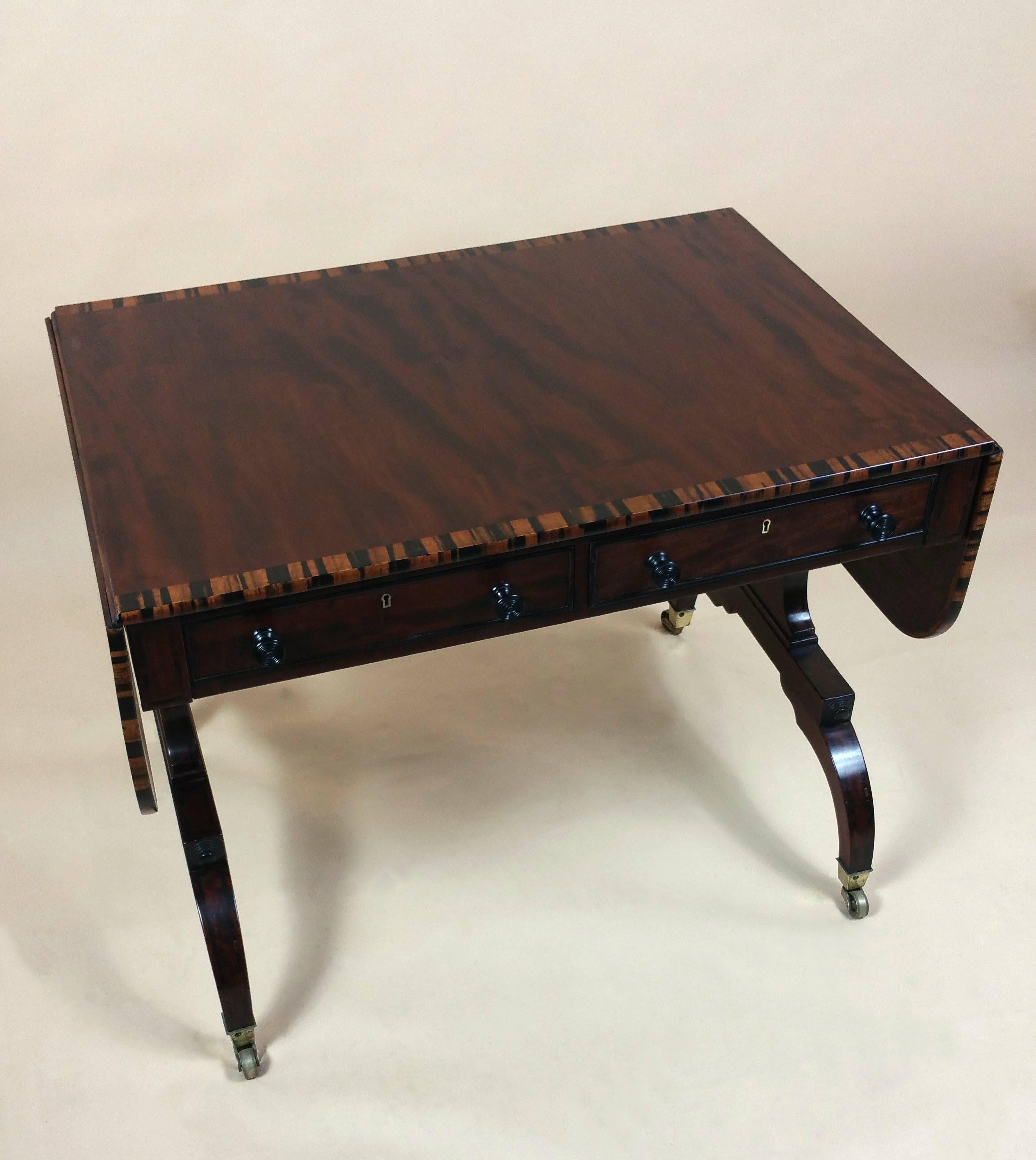 This lovely and fine quality Regency mahogany sofa table features a wide coromandel cross banded and inlaid border with the original ebony handles and turned decoration. The table has two top drawers and stands on original brass feet. It measures 59