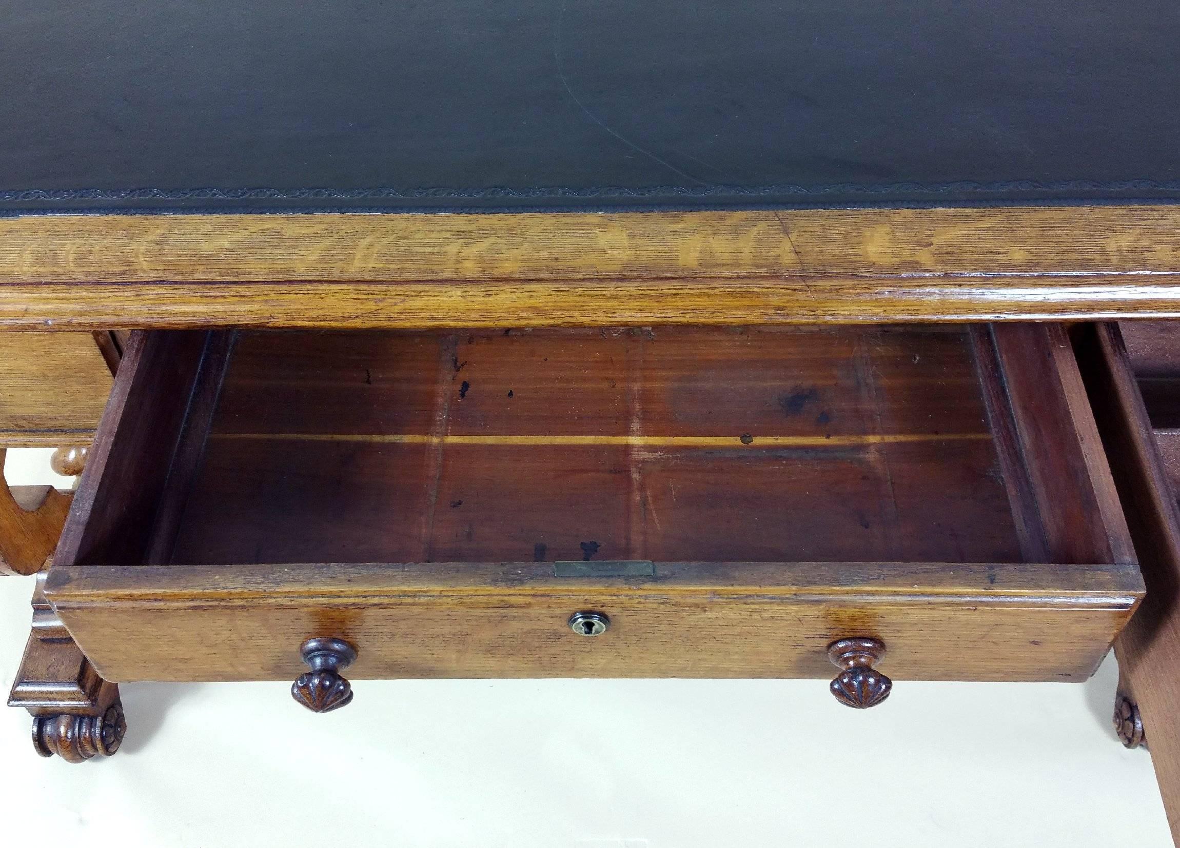 This handsome and excellent quality 19th century oak writing table features three top drawers, one of which has several dividers. The table has a tooled black leather top and leather covered footrest. It also features a lovely bit of carving detail