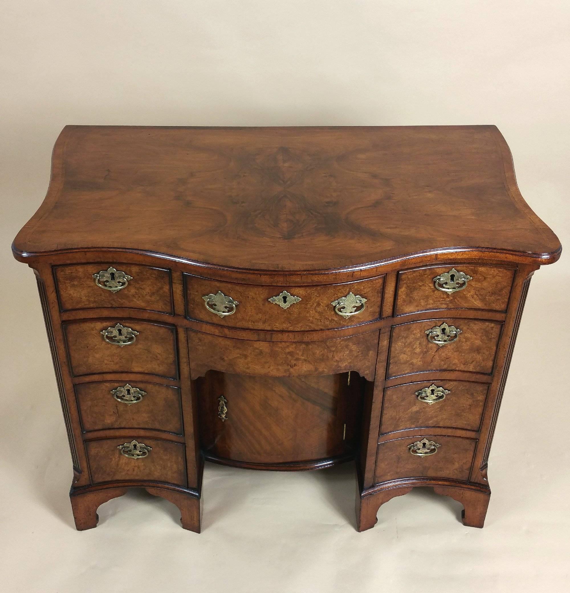 This gorgeous late 19th century figured walnut George I style kneehole desk is fitted with four graduating drawers on each side and a central drawer with a napery drawer beneath. The bow fronted desk features a kneehole set back cupboard, with