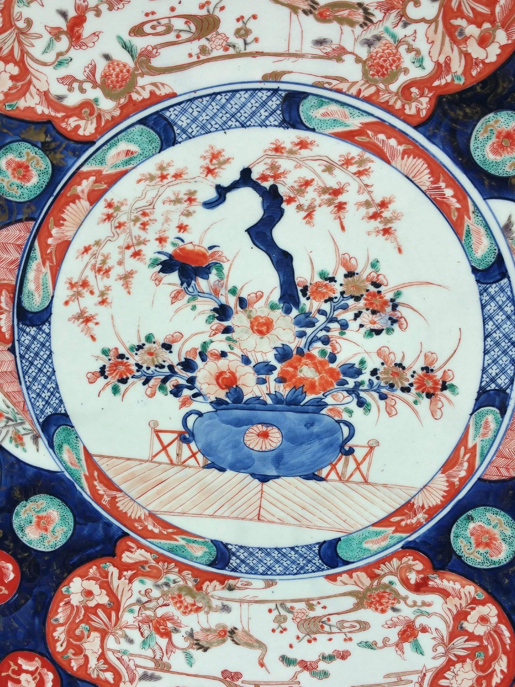 This very large and impressive 19th century Japanese Imari pottery charger plate depicts a central image of a jardinière of flowers surrounded with flora and fauna designs. The charger is of Meji period and also has an oak display stand. It