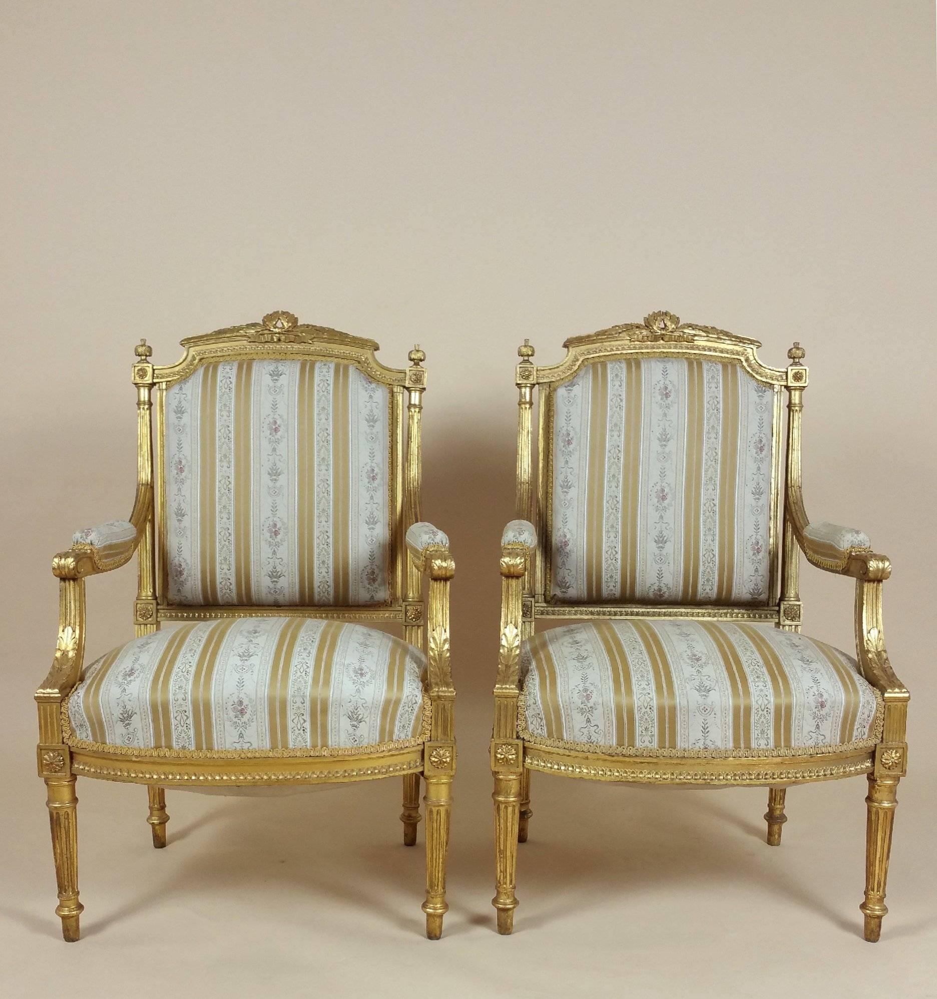 This stunning pair of 19th century French carved giltwood fauteuils are decorated with a design of acanthus leaves, both on the scrolled arms and as a border around the chair. The fauteuils stand on reeded legs and are upholstered in an old gold