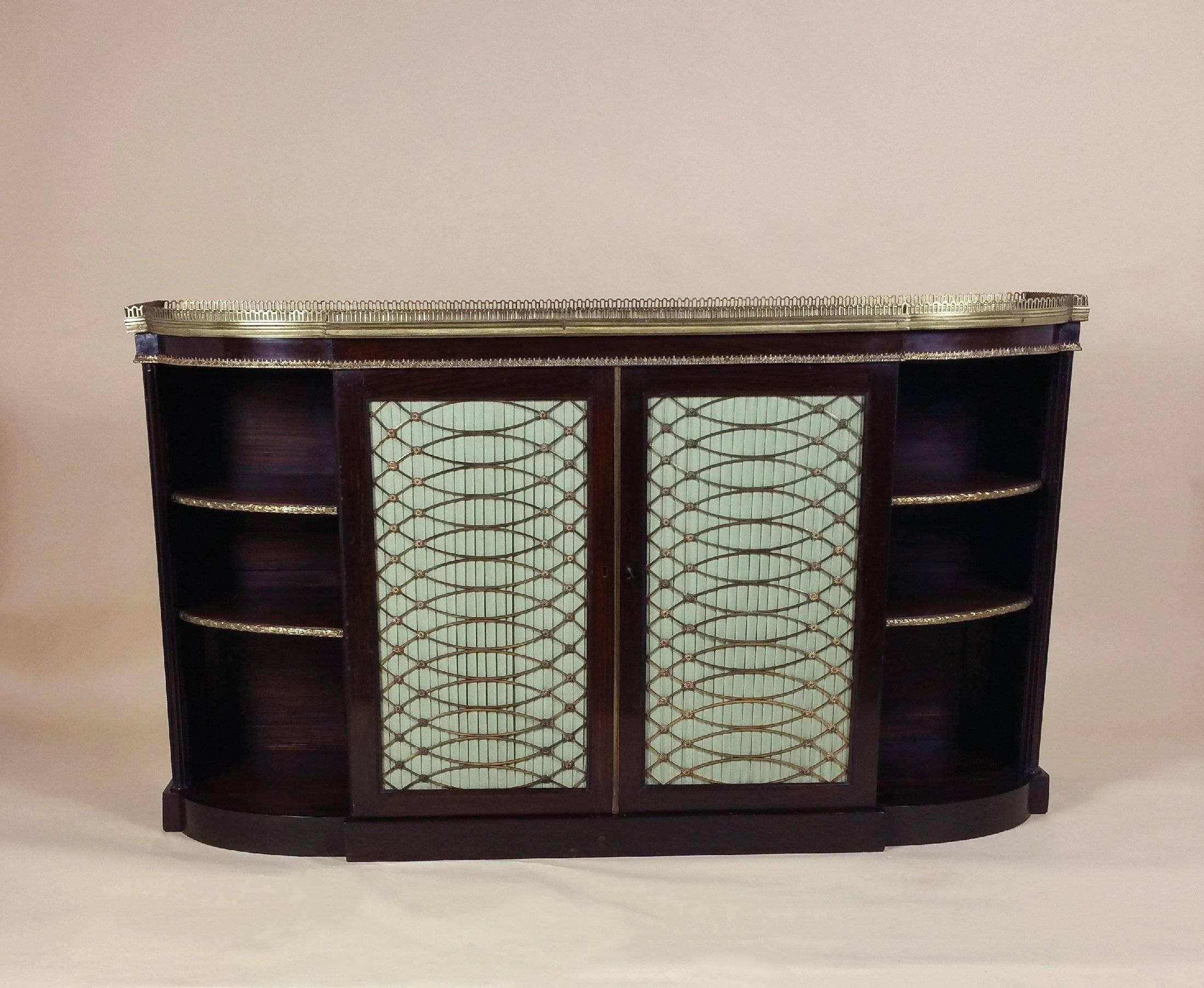 This magnificent Regency period faux rosewood side cabinet features twin brass grill doors lined with pale green pleated silk flanked by open cupboards with two adjustable shelves. The cabinet has a faux marble top with an ornate brass gallery and