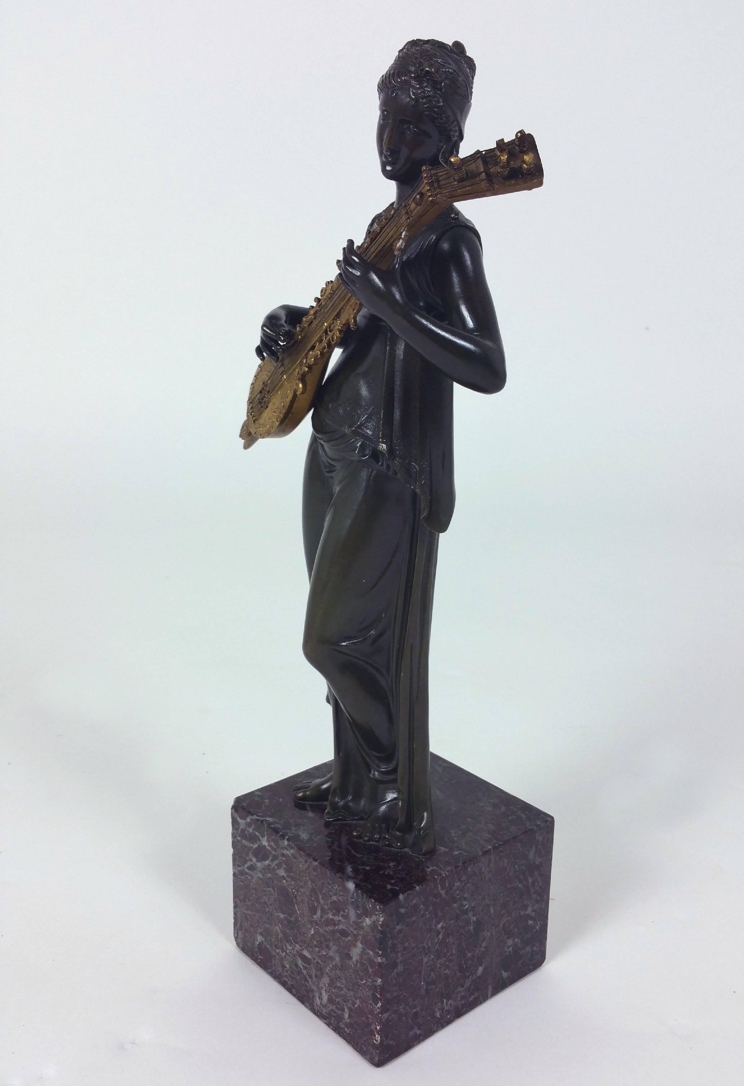 This enchanting 19th century Italian Grand Tour bronze and gilt bronze female sculpture depicts a classical maiden playing an elaborate stringed instrument. The figure is mounted on a square marble cube base and the stringed instrument is gilded. It