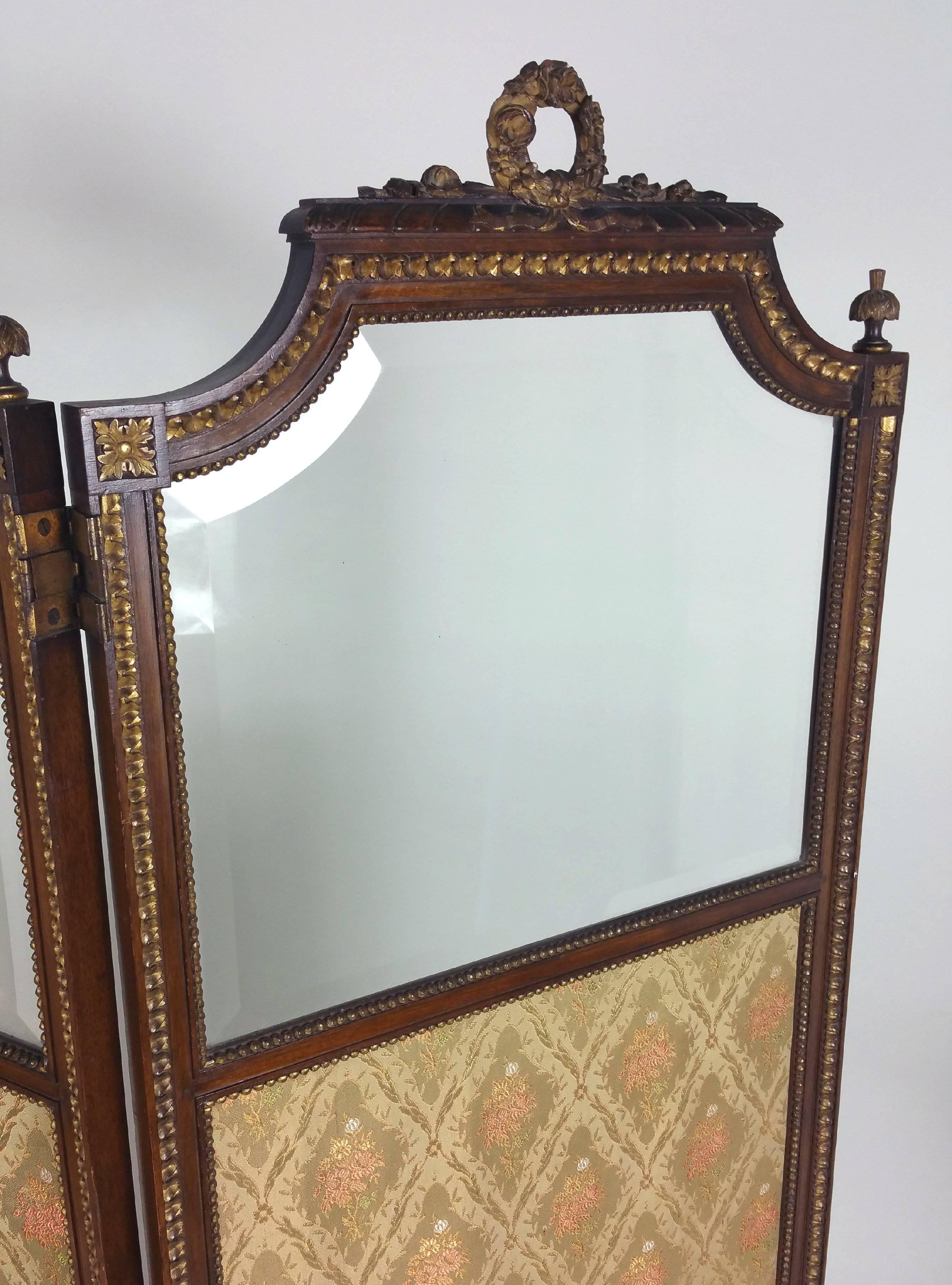 This lovely and delicately designed French carved walnut and gilt three-fold screen is circa 1890 and features the original bevelled glass panels on the top. Each panel has a centrally carved gilt wreath on the top with corner finials and continues