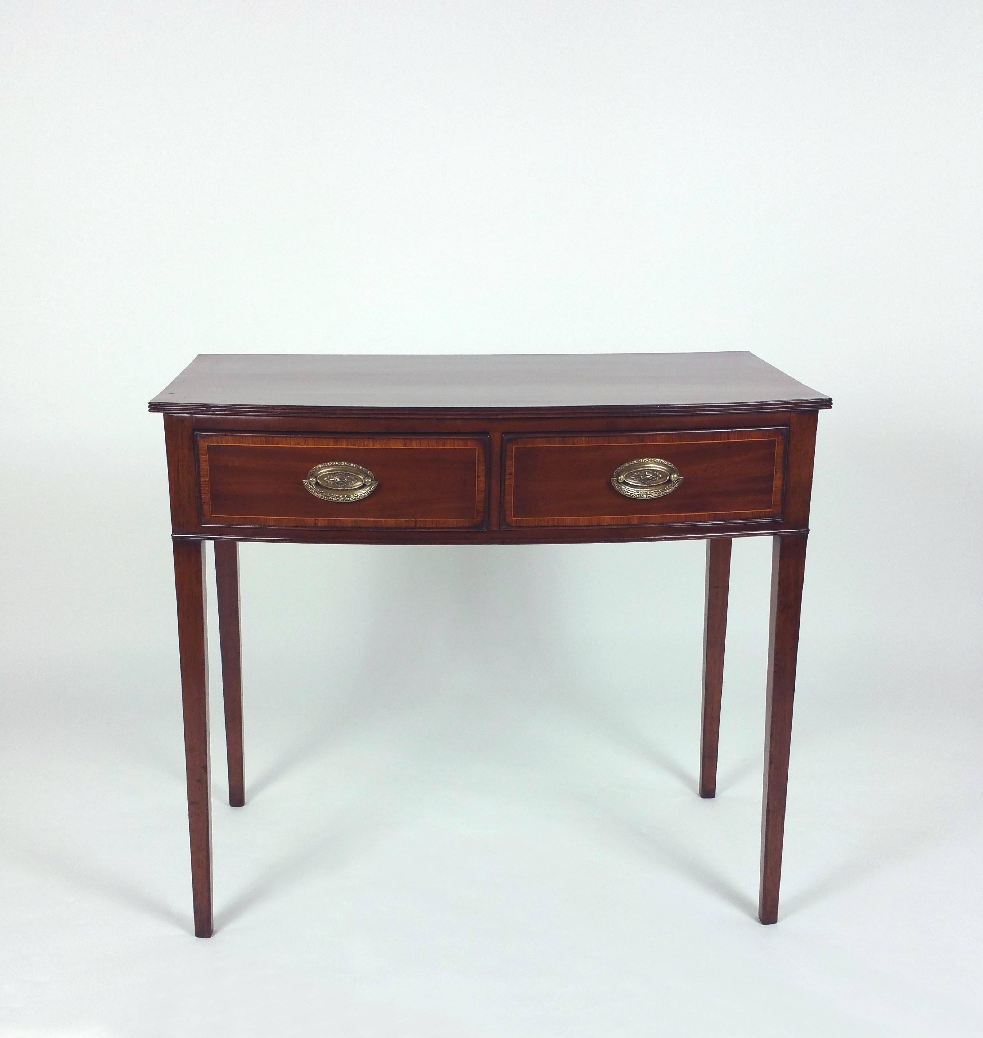 This superb George III mahogany bow fronted two-drawer side table features a rosewood crossbanded decoration around the top and the drawers. The table has decorative brass pull rings for both drawers and stands on square tapered legs. It measures 35