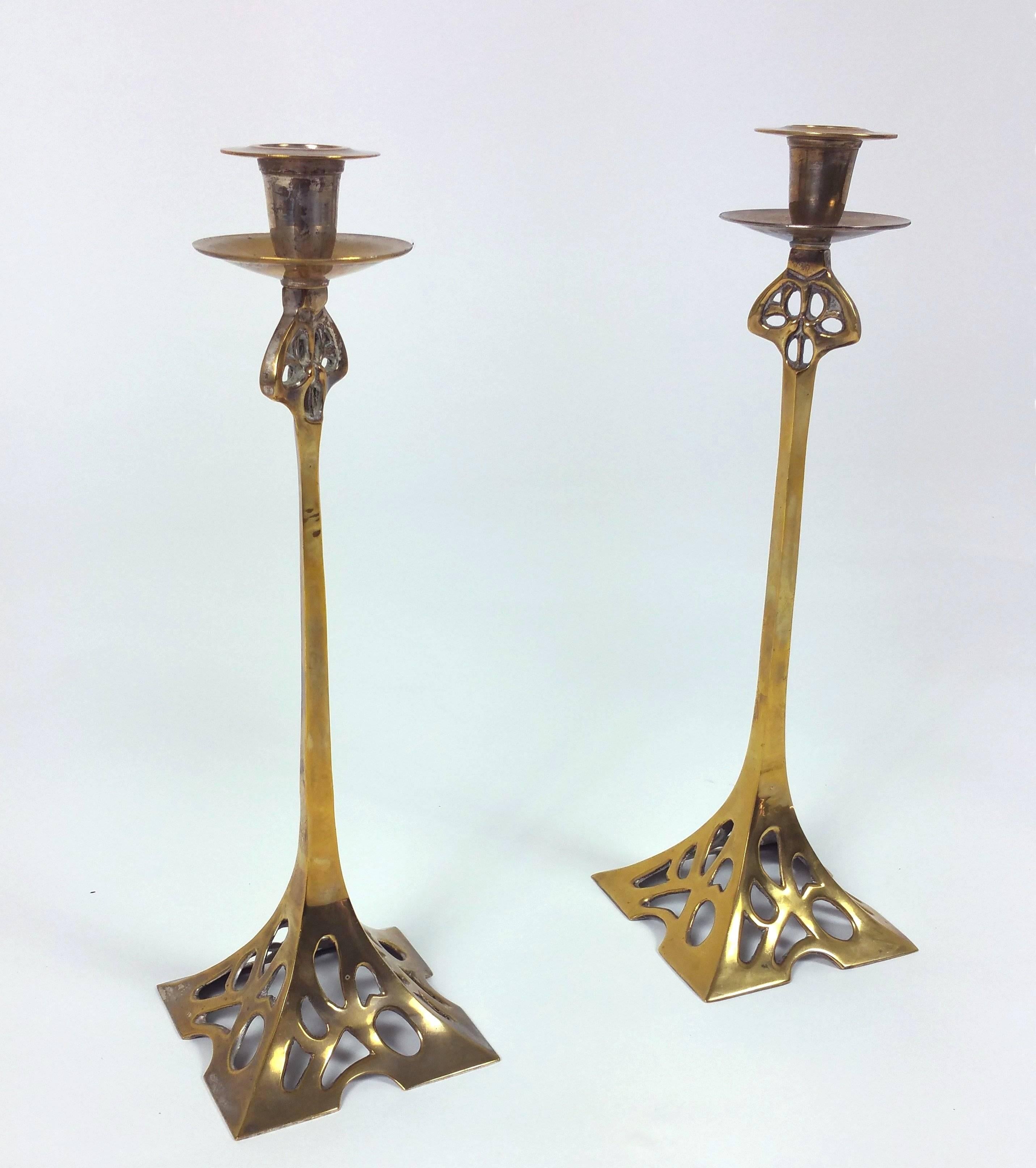 This attractive pair of Art Nouveau 19th century brass candlesticks features a beautifully shaped square base with pierced design detail. Each candlestick measures 4 ½ in – 11.4 cm wide and deep, with a height of 14 ½ in – 36.8 cm. These