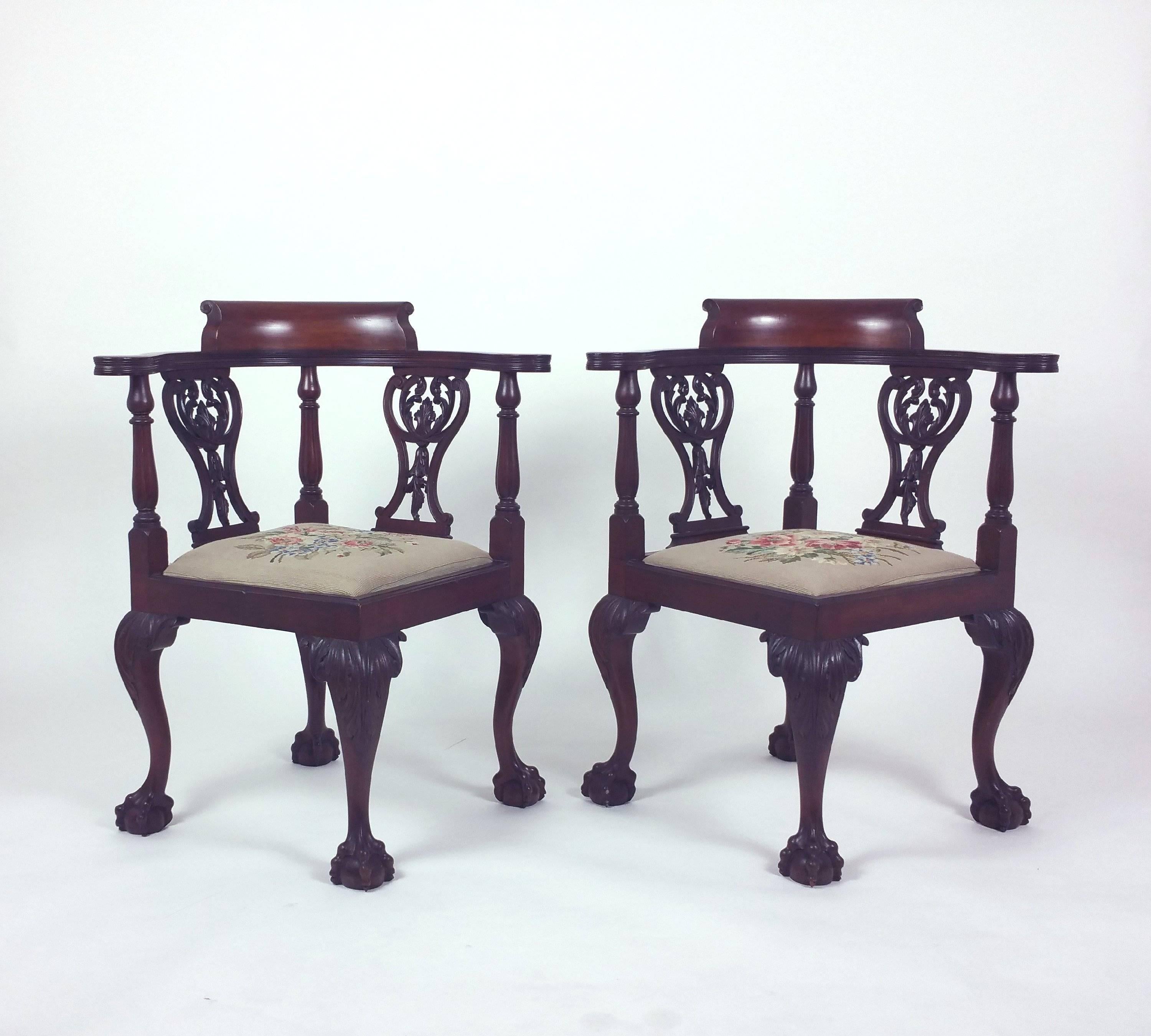 These beautiful and very decorative pair of corner armchairs was designed in the style of Chippendale and features the original needlepoint drop in seats. The chairs stand on ornately carved cabriole legs with ball and claw feet. Each chair measures