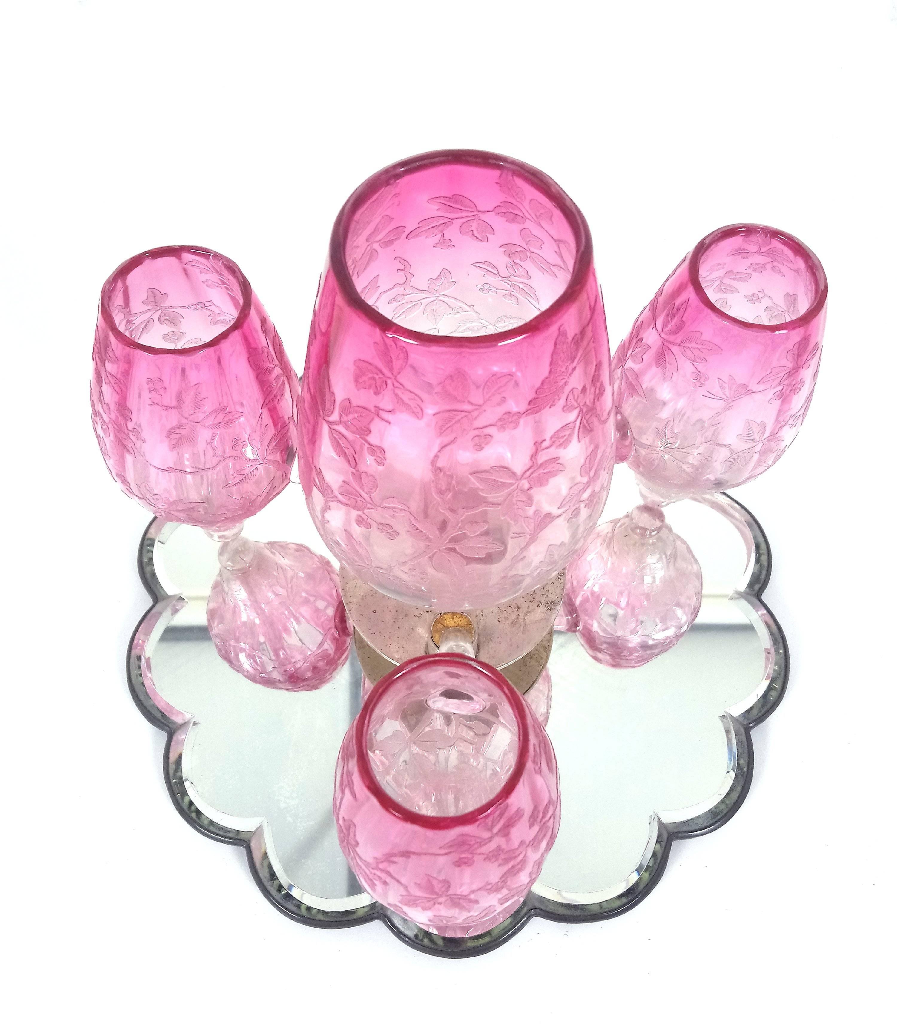 This lovely Victorian engraved cranberry glass four-light revolving table centrepiece has a shaped bevelled mirrored base and features an intricate and delicate design of flowers and trailing leaves. The three smaller glasses are removable so the