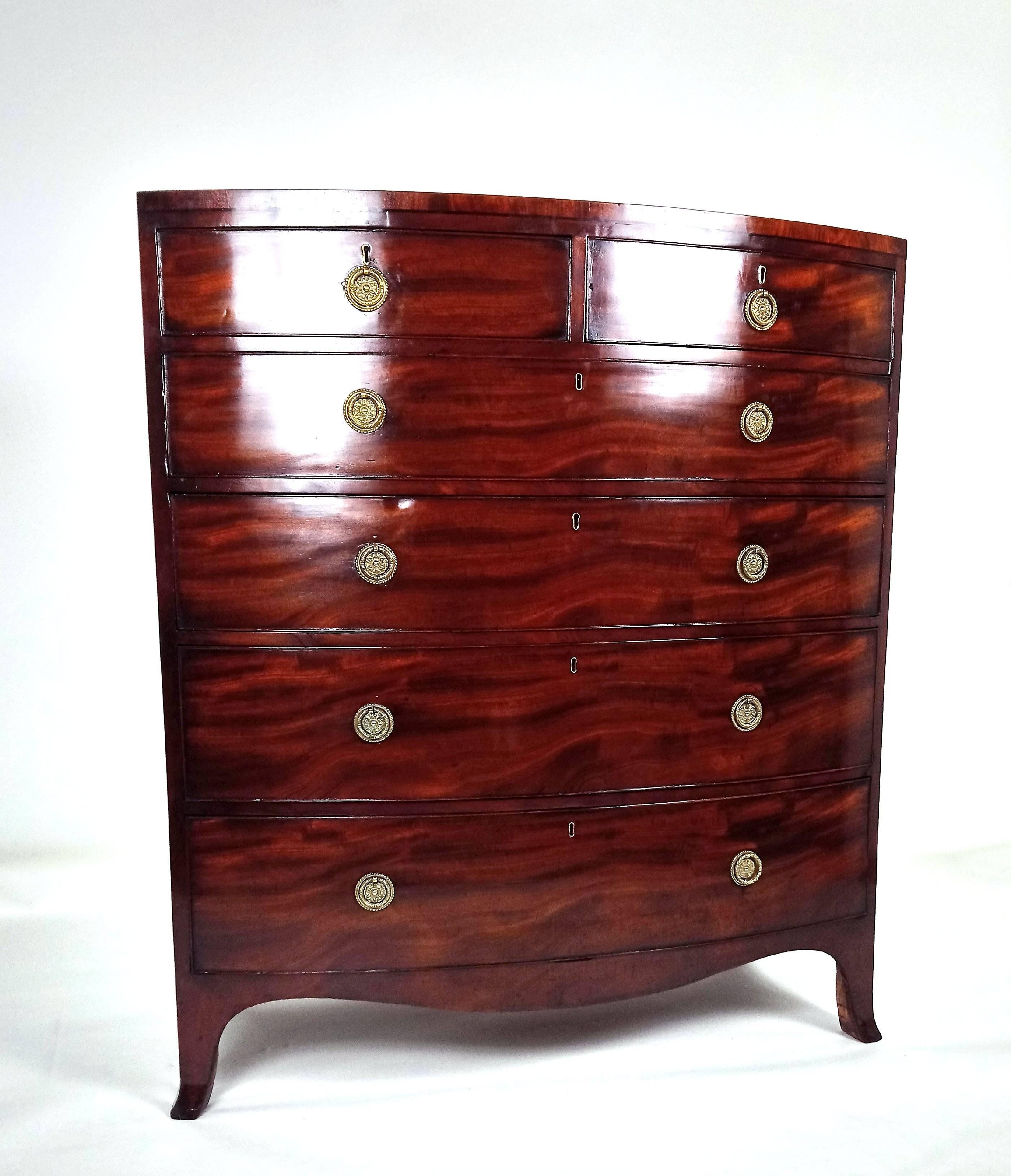 This splendid and very good looking George III figured mahogany bow fronted chest of drawers consists of two short over four long graduated drawers with ornate brass pull rings. It features ebony line inlaid decoration and is oak lined throughout,
