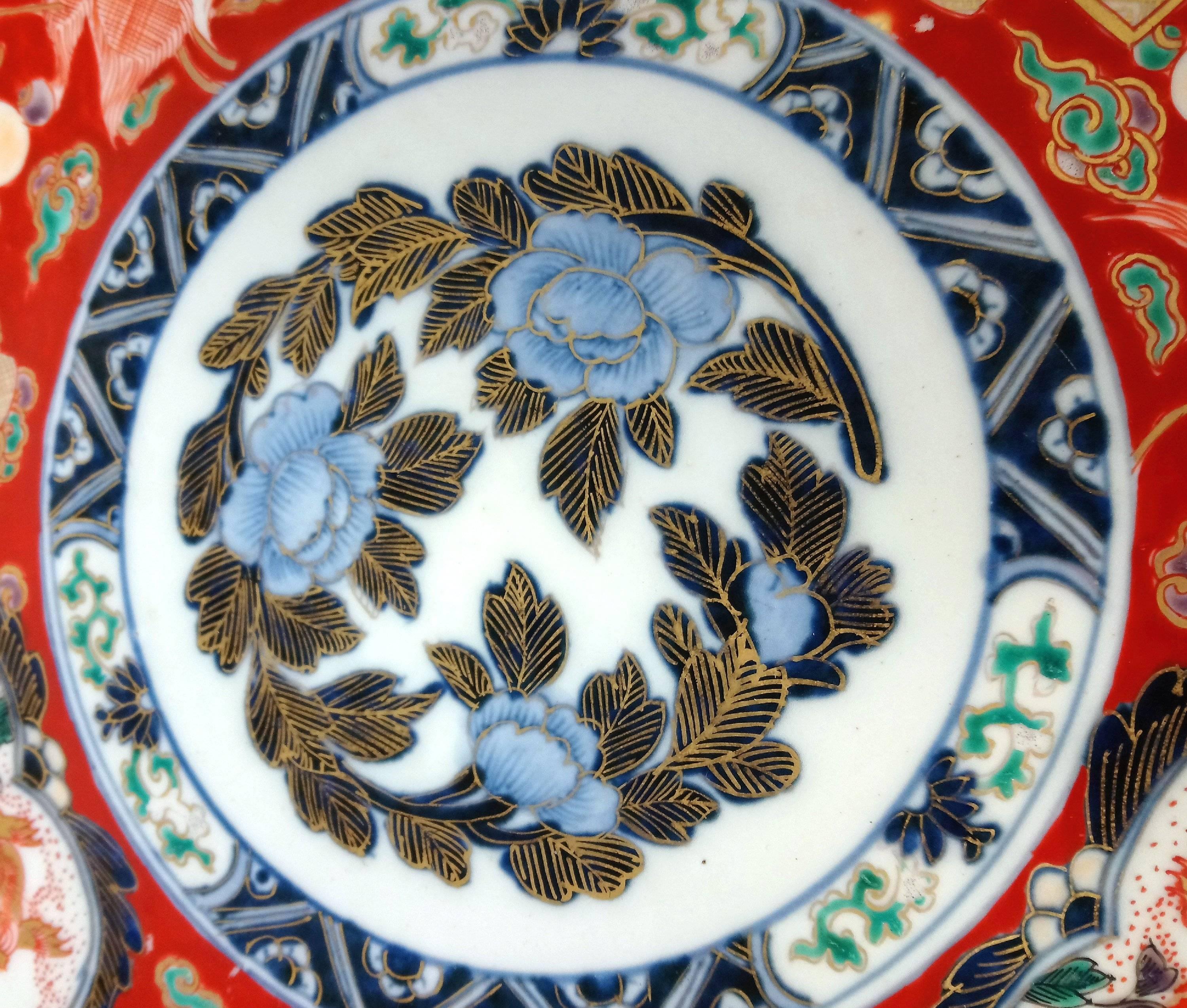 This very attractive and highly decorative 19th century, Japanese Imari pottery dish is painted in predominately red enamels with gilt highlights depicting flying cranes, temple dogs and precious objects surrounding a central medallion of flowers.