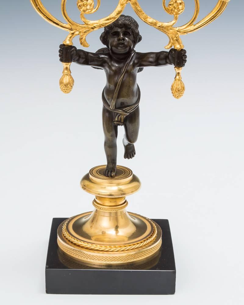 A fine pair of knurled ormolu bases mounted on black marble plinths supporting bronze cherub figures issuing two ormolu and bronze candle nozzles.

The casting and details of the metalwork is exceptionally fine.
 