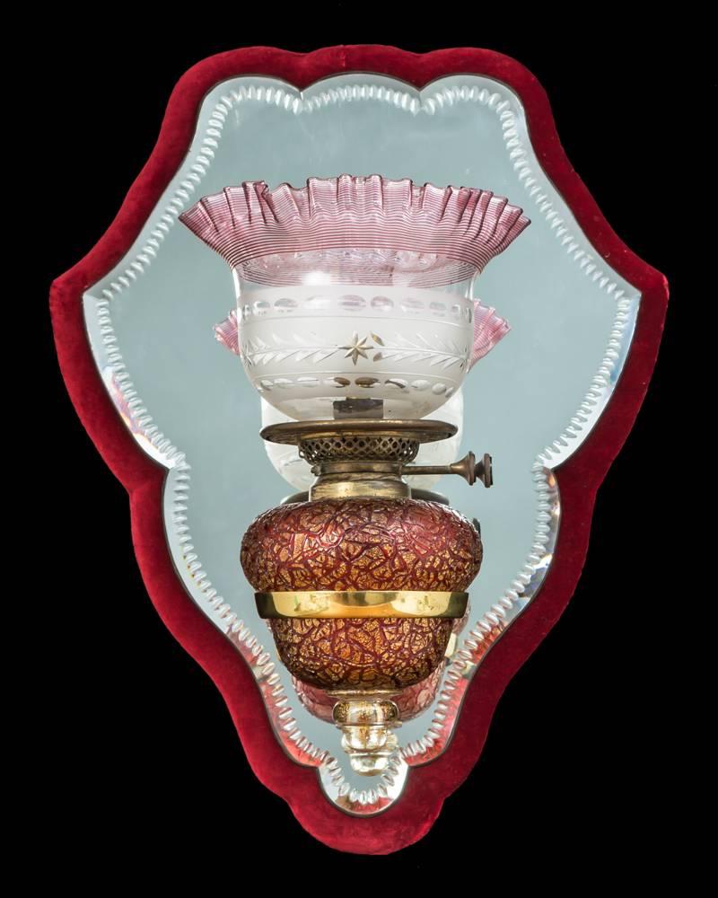A pair of notch cut mirrors mounted on crimson velvet borders this issuing a gilt bronze arm mounting a highly unusual gilt and crimson crackled glass oil fount still with its burners this mounting a frosted and cut-glass shades with crimson