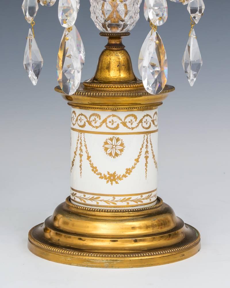A pair of Georgian candlestick the gilt lacquered bases with ball bead knurl mounting white porcelain drums with gilt decoration this supporting diamond cut-glass eggs terminating with van dyke pans and nozzles hung with double pointed spangles and