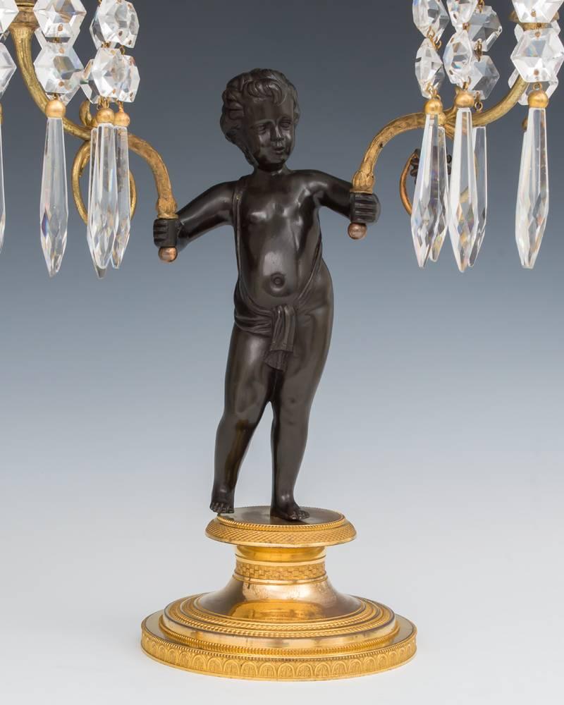 An exceptional pair of Regency period gilt bronze cherub candelabra, the mercurial gilt bases with finely knurled decoration, the bases surmounted with a finely cast bronzed cherub with outstretched arms holding finely chased ormolu and bronzed