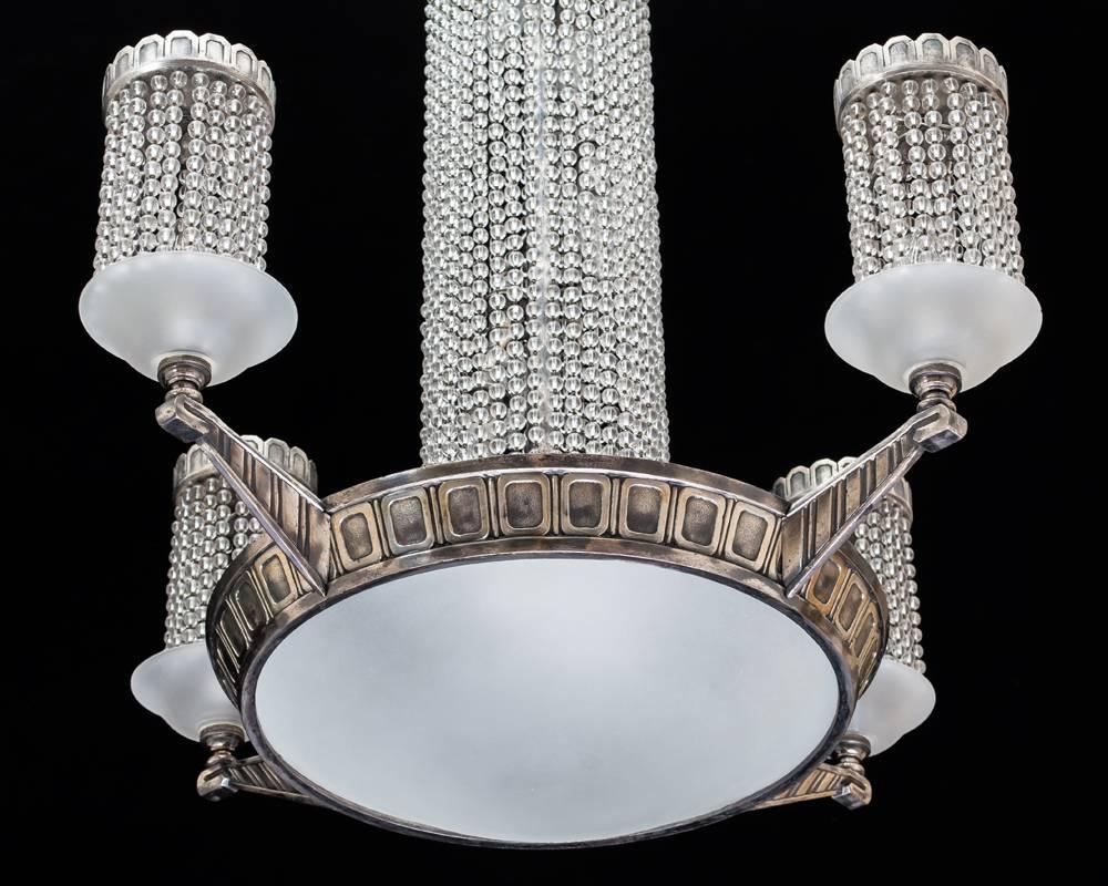 The main silver band with pillar and rectangular decoration this with frosted glass under dish the band issuing four lights also with under dishes and arched decoration the chandelier hung with strings of beads.