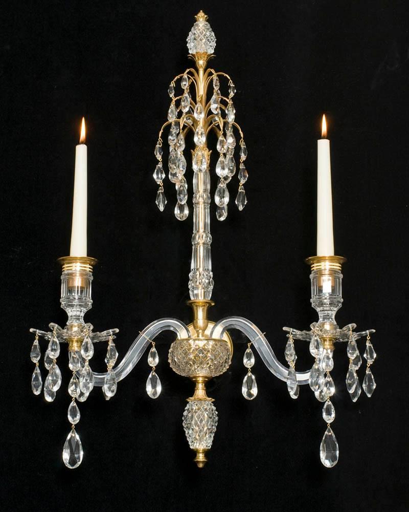 A fine pair of ormolu-mounted cut-glass two-light wall-lights in Adam styles the central diamond and slice cut-glass column surmounted by three drop hung ormolu sprays and a ormolu-mounted diamond cut-glass egg, the ormolu back plate surmounted with