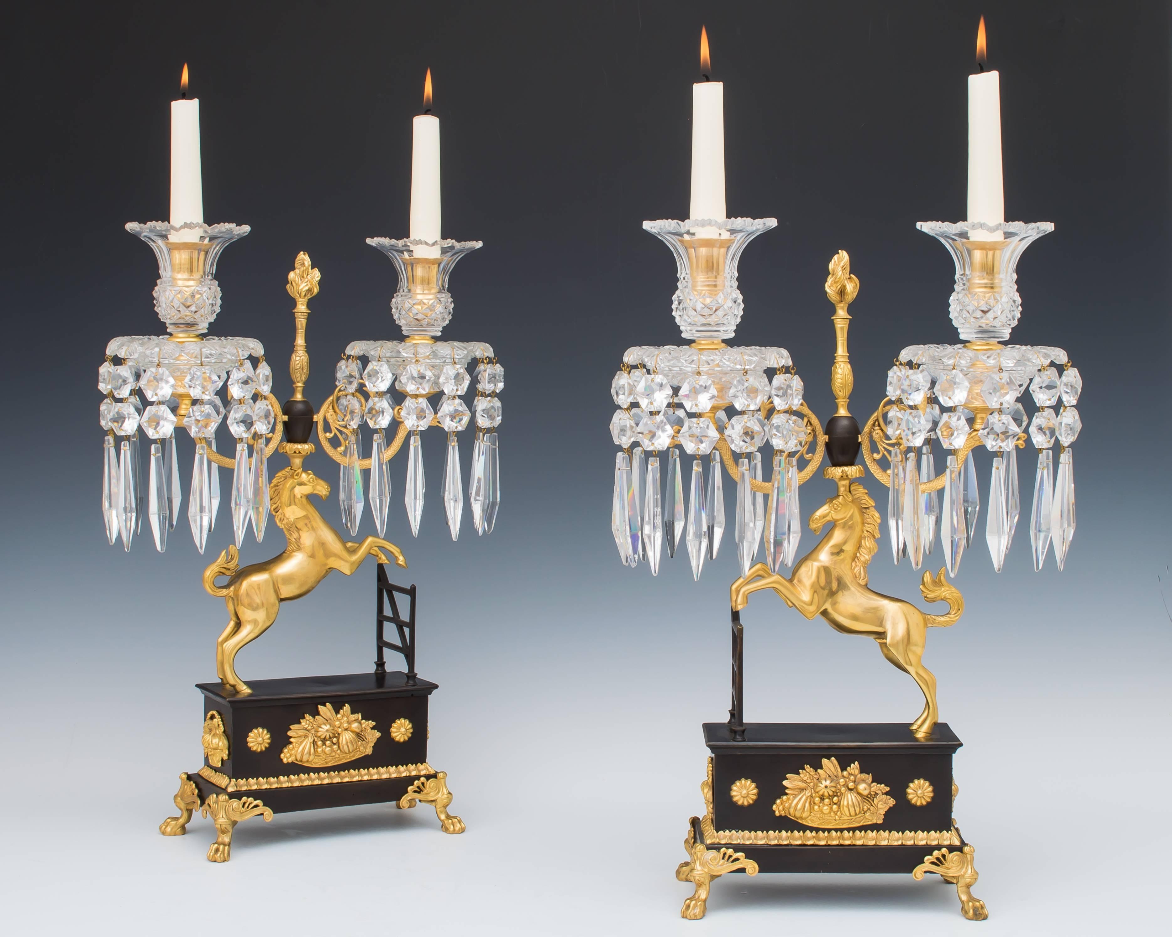 An unusual pair of Regency period ormolu and bronze mounted cut-glass candelabra the bronzed rectangle bases are finely mounted with lion paw feet, basket of fruit and flowers these bases surmounted with a gilt horse jumping towards a bronzed gate