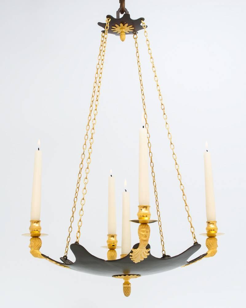 A fine five-light Empire chandelier the bronze body issuing a central candle nozzle and four Gothic heads supporting candle nozzles and drip pans this suspended on four ormolu chains from the bronze canopy both the canopy and body having the same