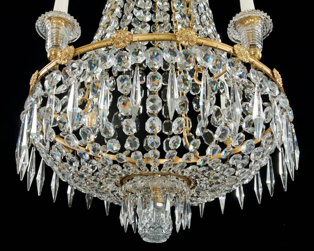 The knurled and flower rosette decorated ormolu band surmounted with four diamond the step cut turnover top candle nozzles the chandelier of Classic tent and basket design all hung with rectangular eight sided spangles and triangular icicle drops.