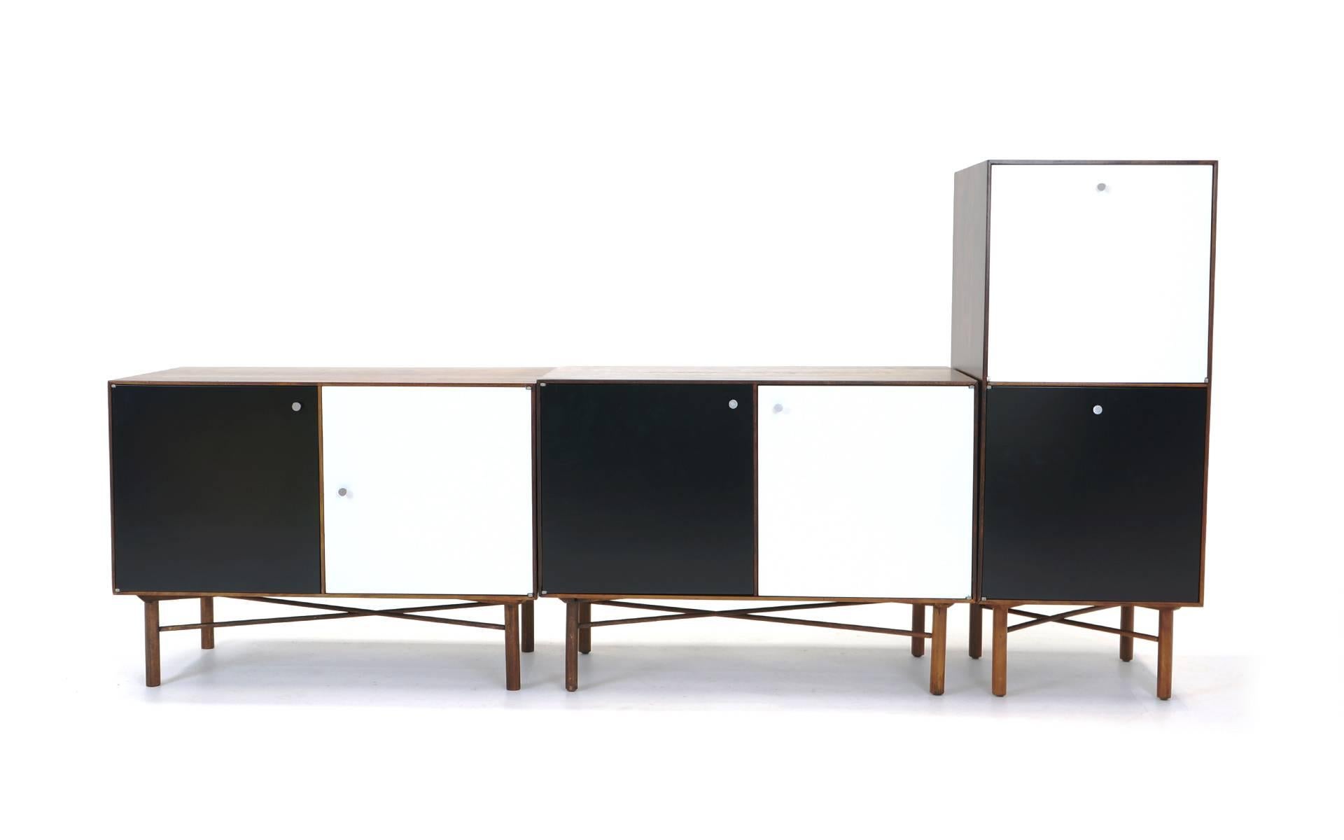 Five modular walnut cabinets with black and white lacquered doors and original pulls, with dowel legs and X-cross stretchers. Two vertical cabinets and three horizontal cabinets. Each cabinet consists of two storage compartments. Each compartment