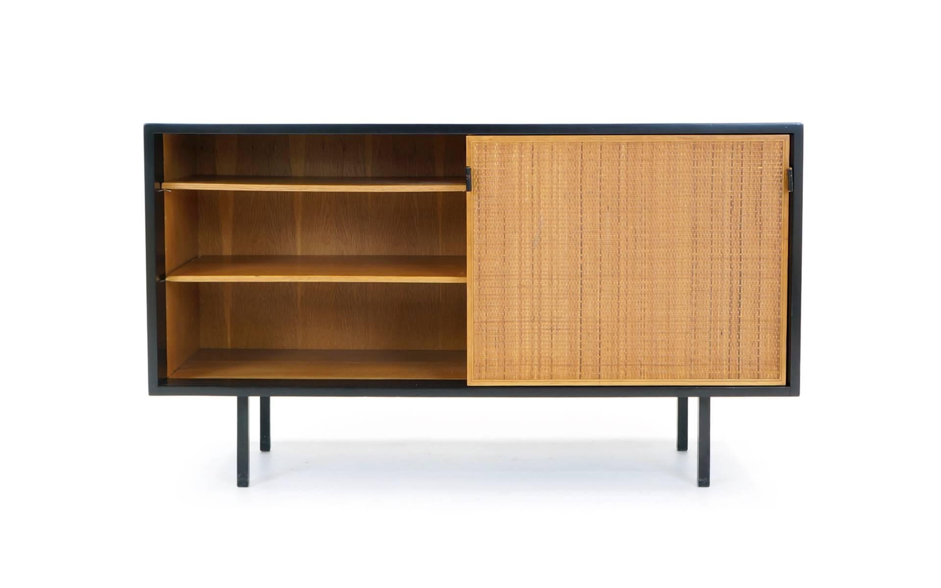 Beautiful early design by Florence Knoll for Knoll. Cabinet features sliding doors with leather pulls revealing two adjustable shelves on one side and one adjustable shelf on the other. There is a round hole cut-out of the back of the right hand