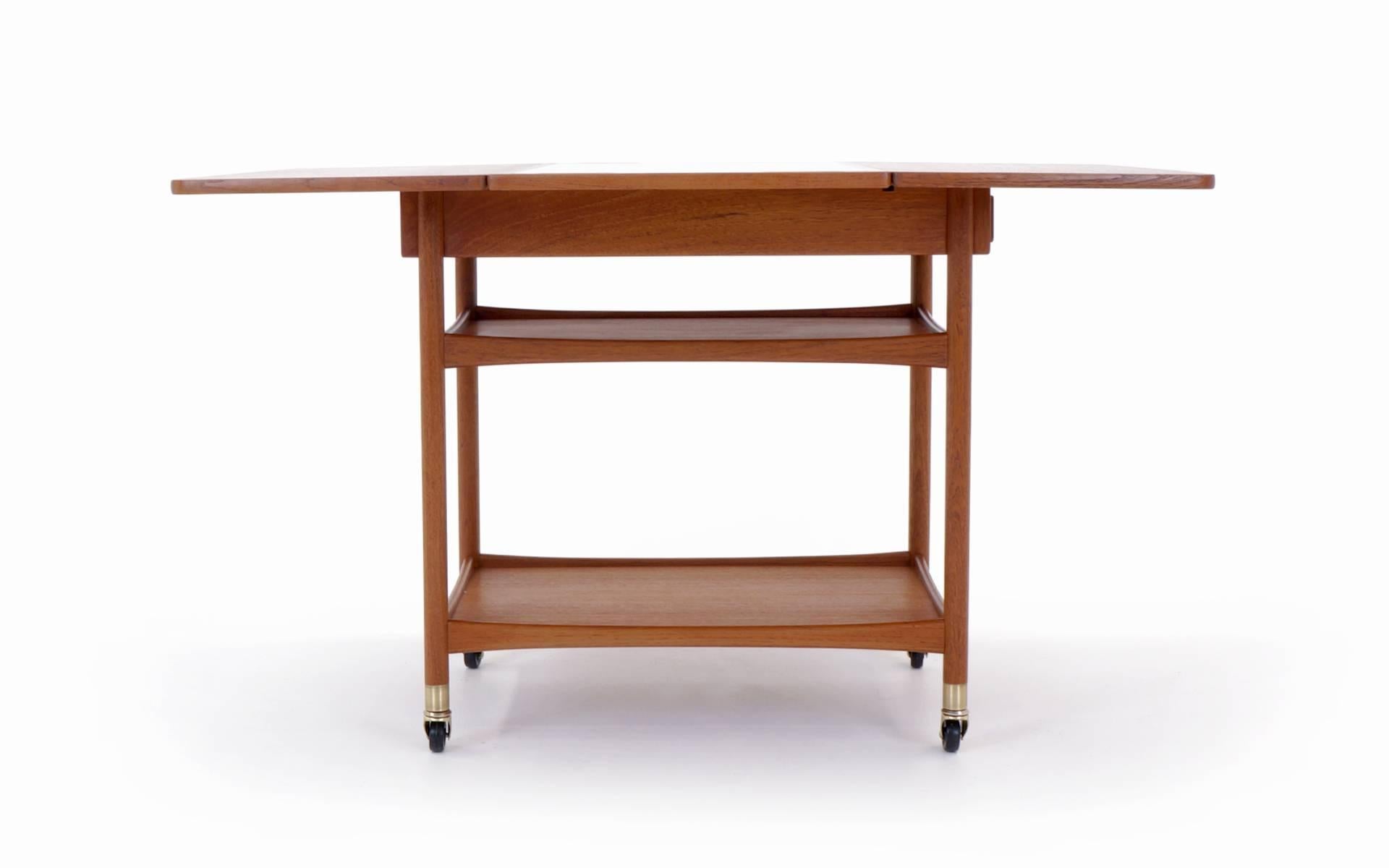 Versatile and unique Danish bar cart or serving cart with teak drop leaves and black laminate center surface. When you raise the leaves the top swivels to support the leaves. A very sophisticated design. Collapsed width is 17.75 in. extended width