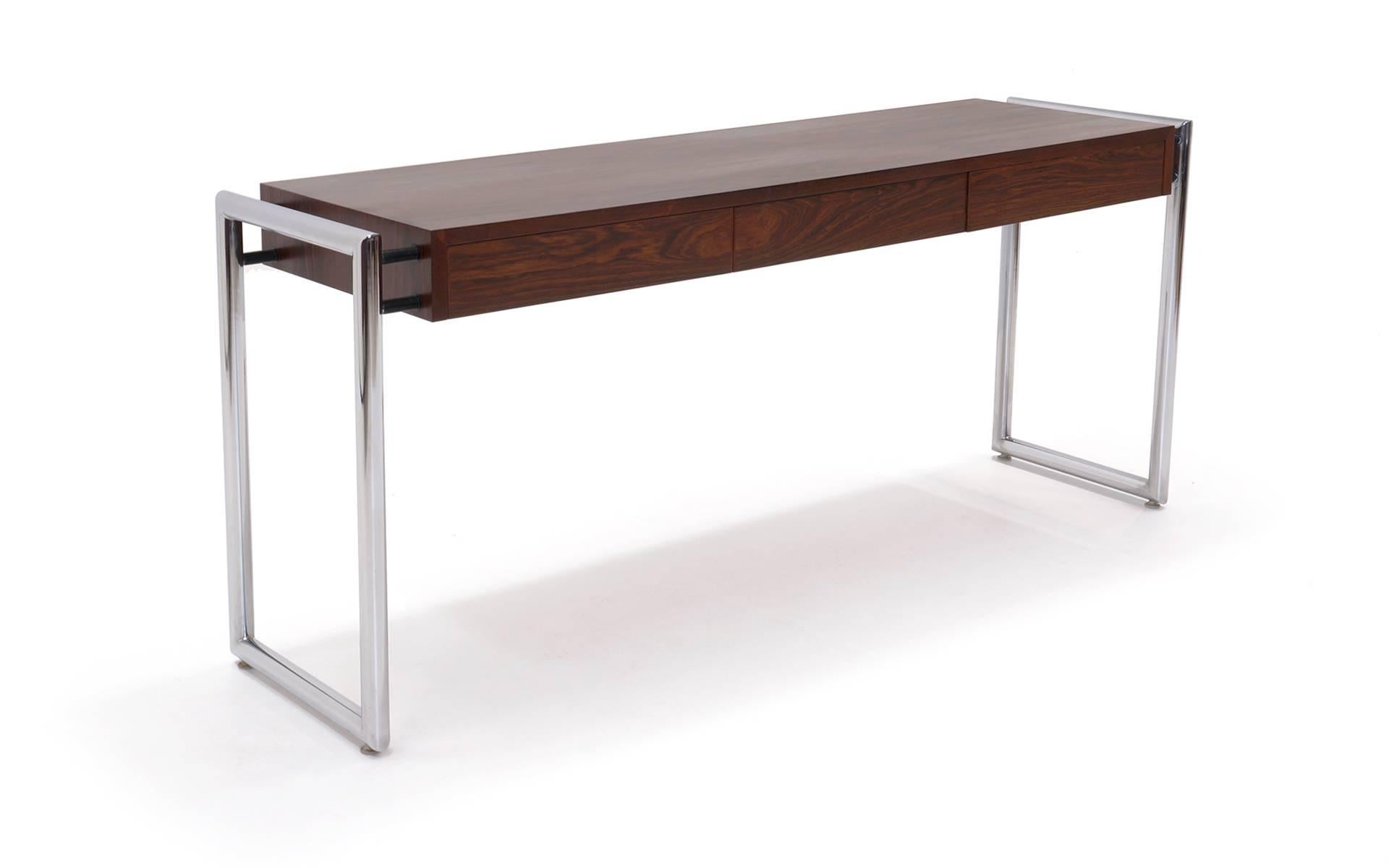Long and sleek, this beautifully patterned Brazilian rosewood desk is a rare design by Milo Baughman. A tubular chromed steel rectangular frame attaches with horizontal threaded members so the three drawer desk floats within the frame.