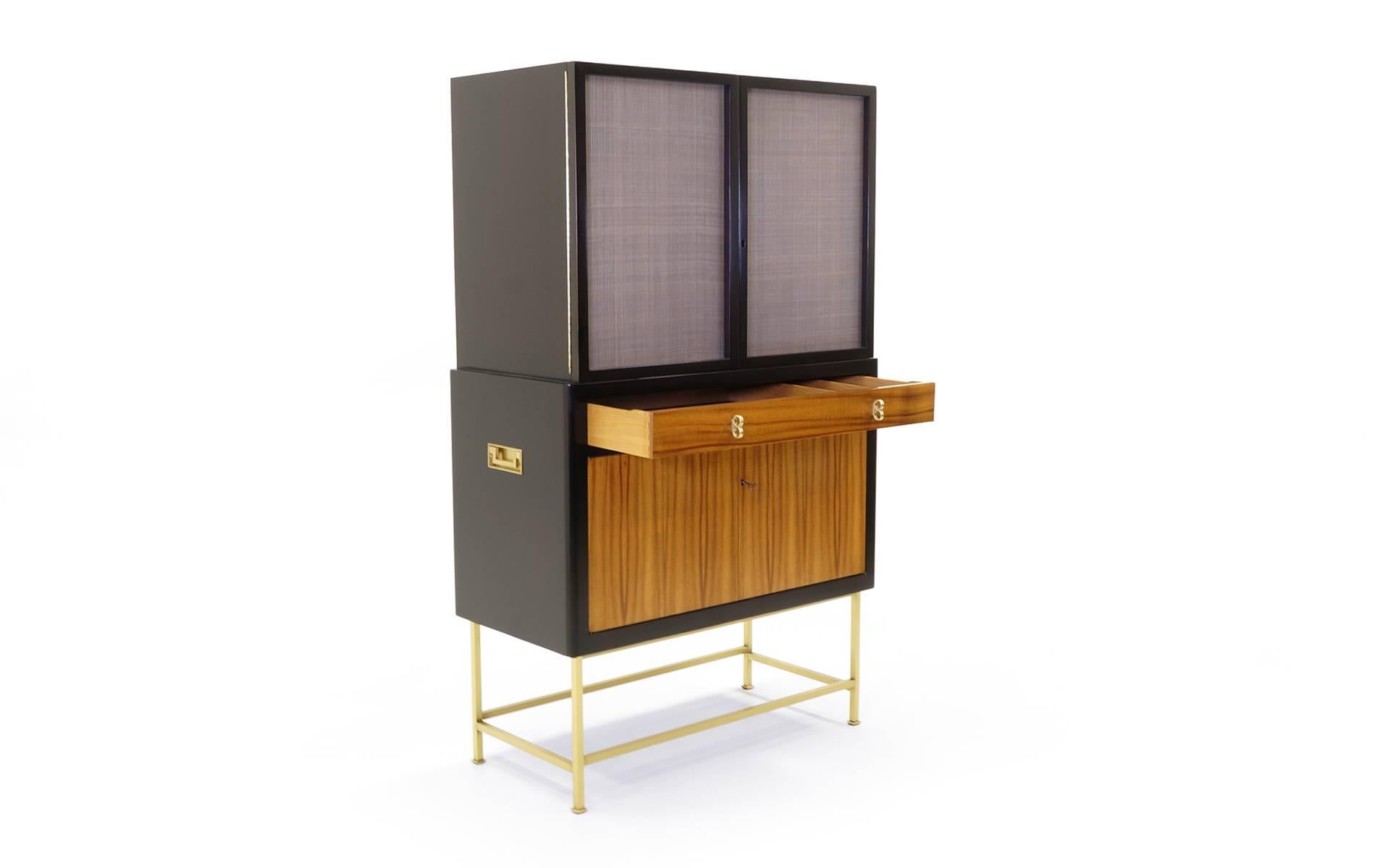 Exceptional Edward Wormley for Dunbar bar cabinet. Large-scale cabinet of dark and bleached African mahogany on a base of solid brass tubing. The upper cabinet is lighted and features locking doors with two adjustable glass shelves. The upper doors