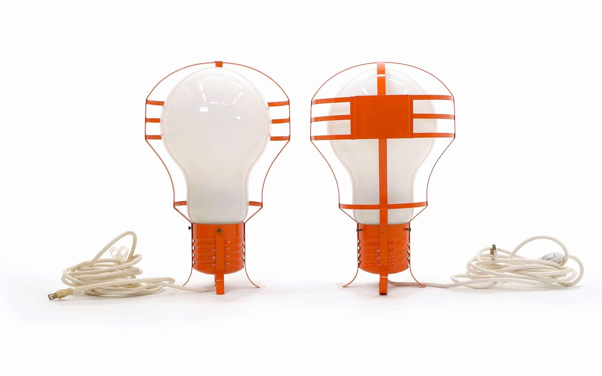 Striking pair of 1960s Italian oversized light bulb lamps. These can stand on end on their side or can be hung by the white cord. Orange lacquered steel frames over the glass bulbs give the look of an Industrial work lamp.