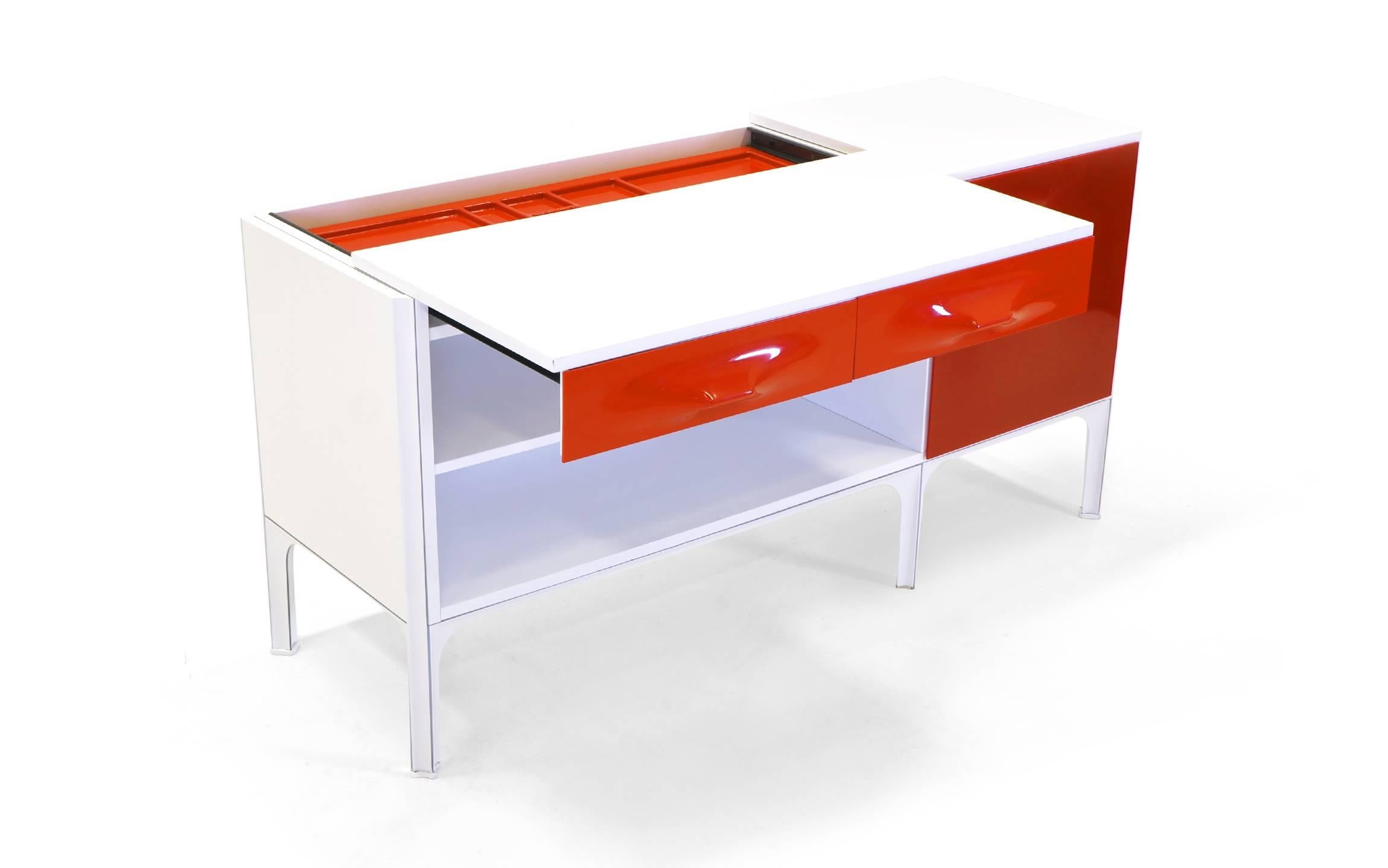 Rare Raymond Loewy DF2000 desk in red, orange, and white. See photos for how the desk top slides forward to create clearance for a chair and also reveals storage. Red molded plastic door reveals three orange lacquered wood drawers. Steel frame.