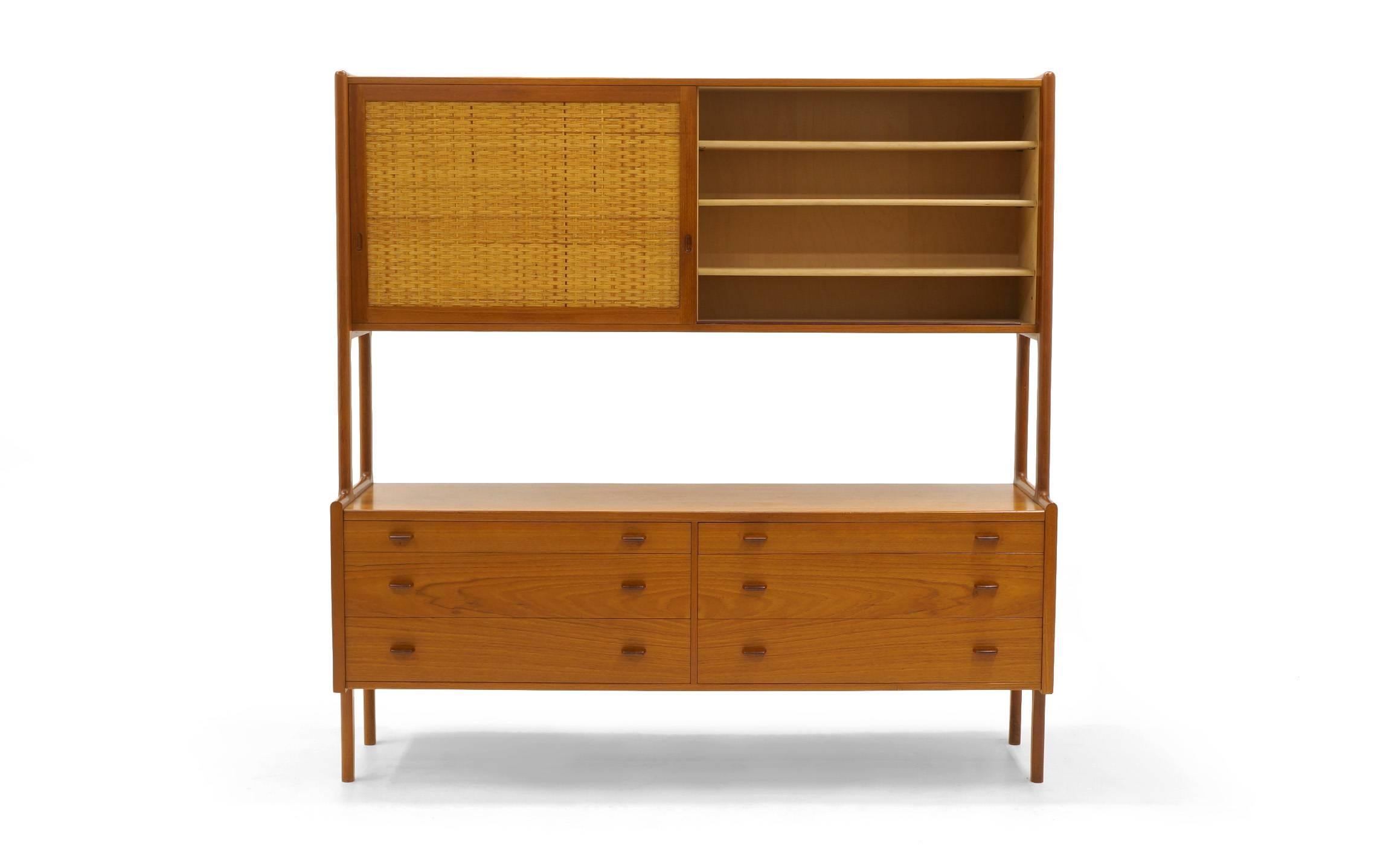 Excellent original condition Hans Wegner storage cabinet in teak. Sliding cane covered teak sliding doors on top reveal adjustable shelves (three on one side, two on the other). Top two drawers on lower portion have new felt lining. This unit is in
