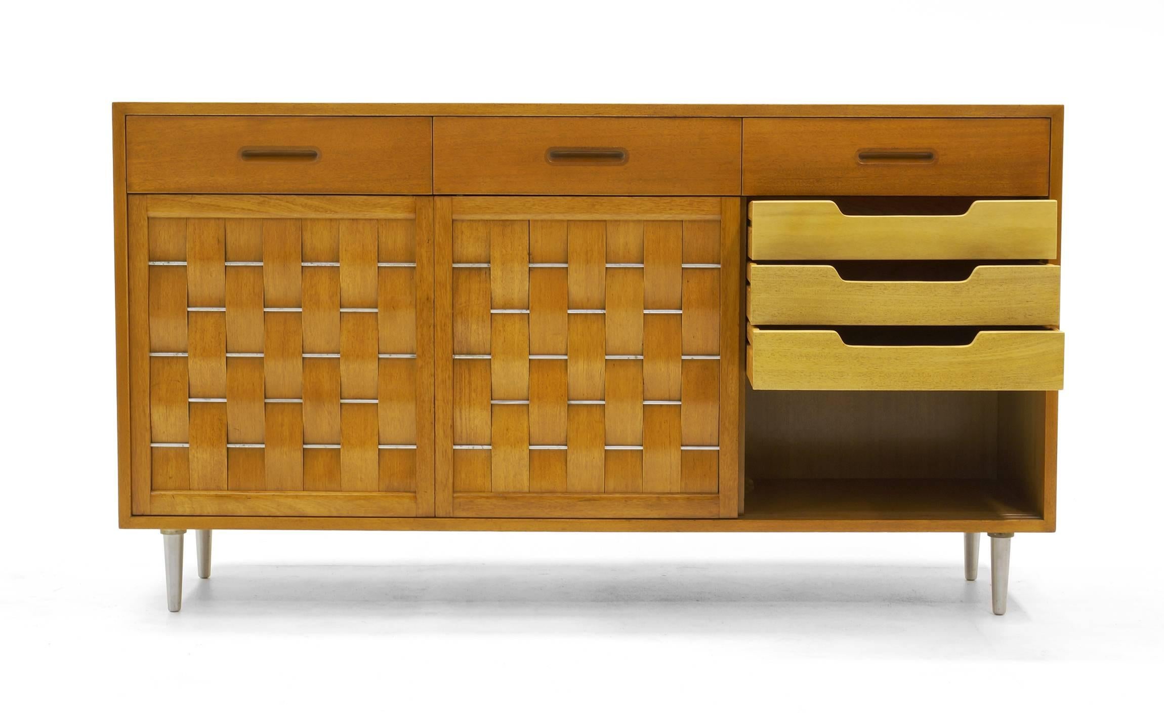 Edward Wormley three-panel woven front credenza/buffet. Bleached African mahogany with solid brushed aluminum conical legs and rods. Expertly restored and refinished.