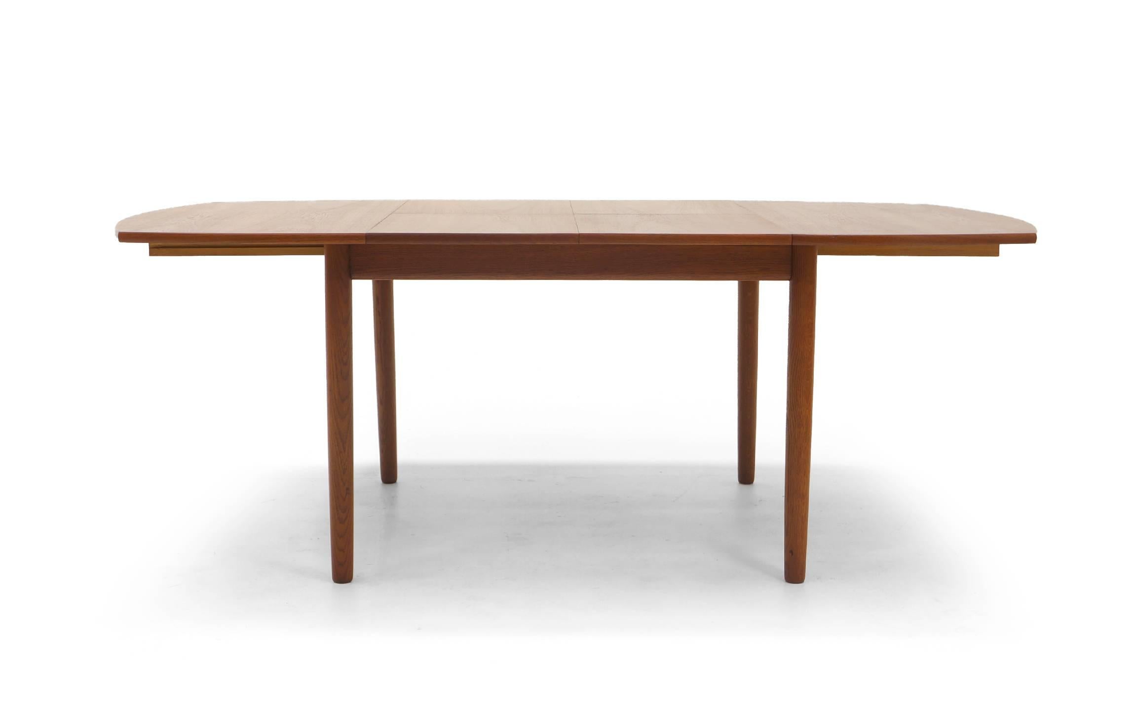 Teak dining or kitchen table designed by Ejner Larsen and Aksel Madsen. Ingenious design featuring two leaves permanently stored inside the table. The table begins as a 45 inch square with subtle curved ends and when expanded reveals two stored