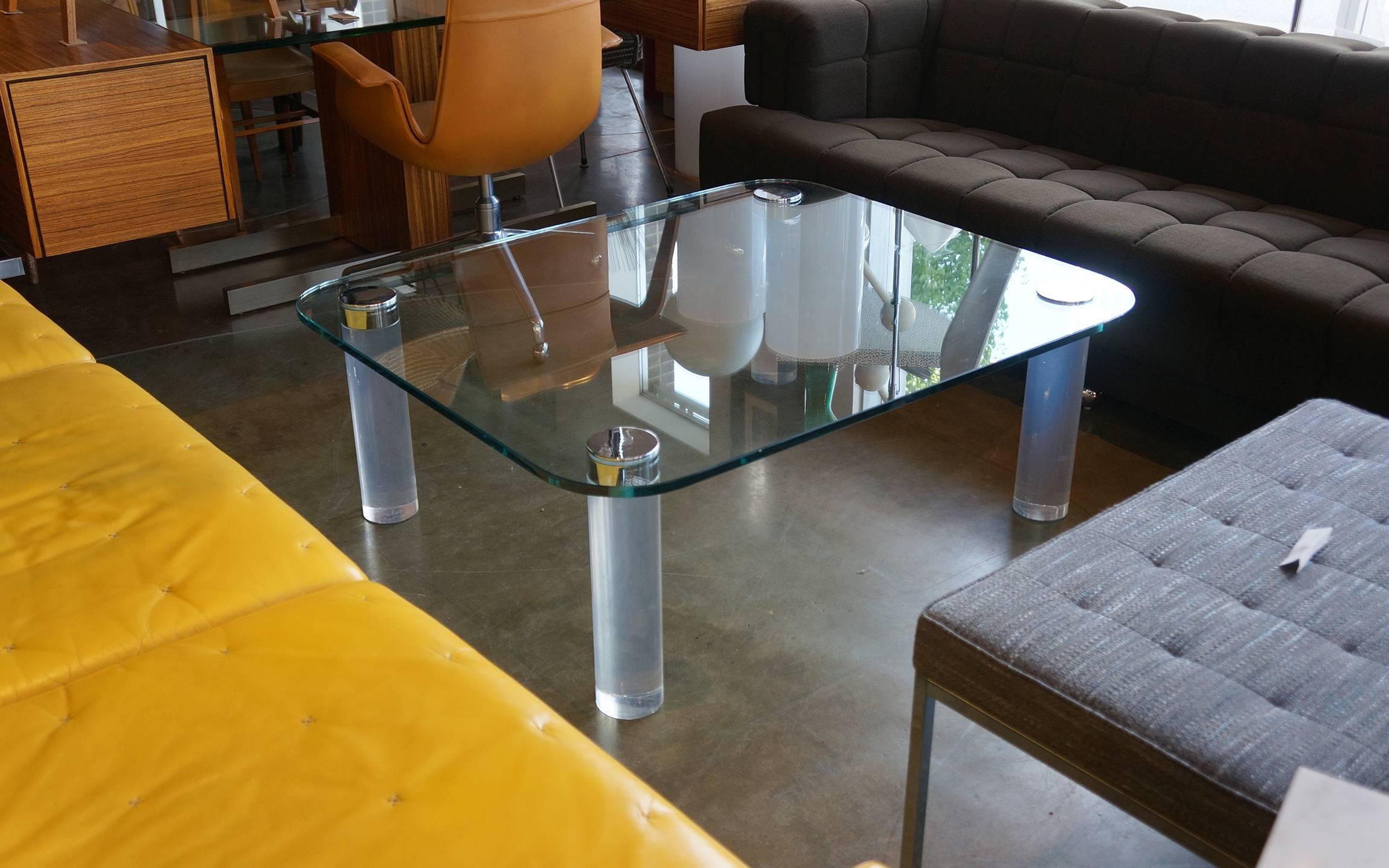 Large, almost square, but actually rectangular, coffee table possibly designed by Karl Springer. The glass has zero chips or imperfections and only minor surface wear. The solid heavy chromed steel round caps screw into the acrylic legs through