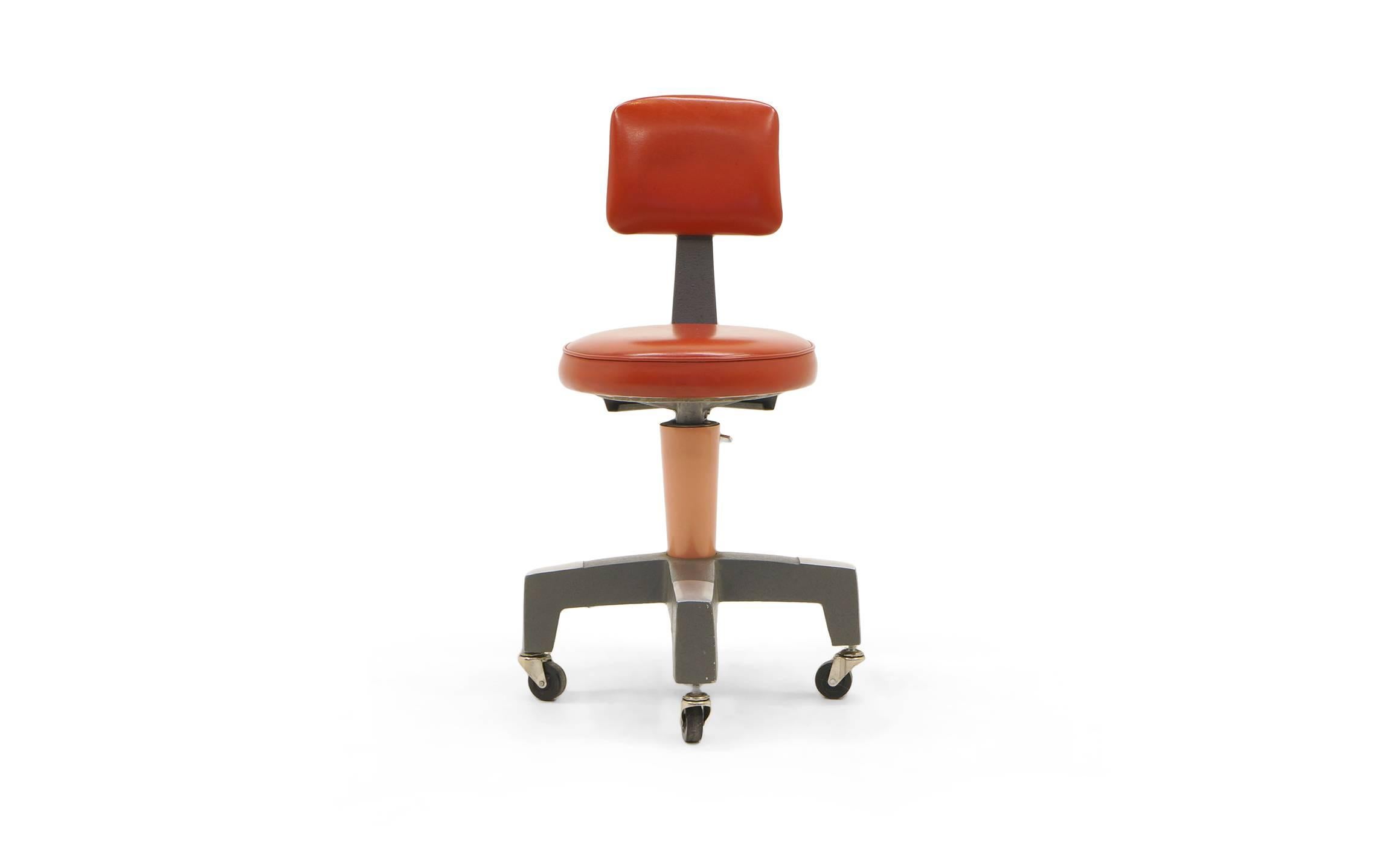 1950s Industrial Design work chair on casters, also swivels. One of the coolest designs we have seen. Would make a great desk chair. Model number 14090 by the American Optical Corporation. The red-orange vinyl is in excellent condition with no tears