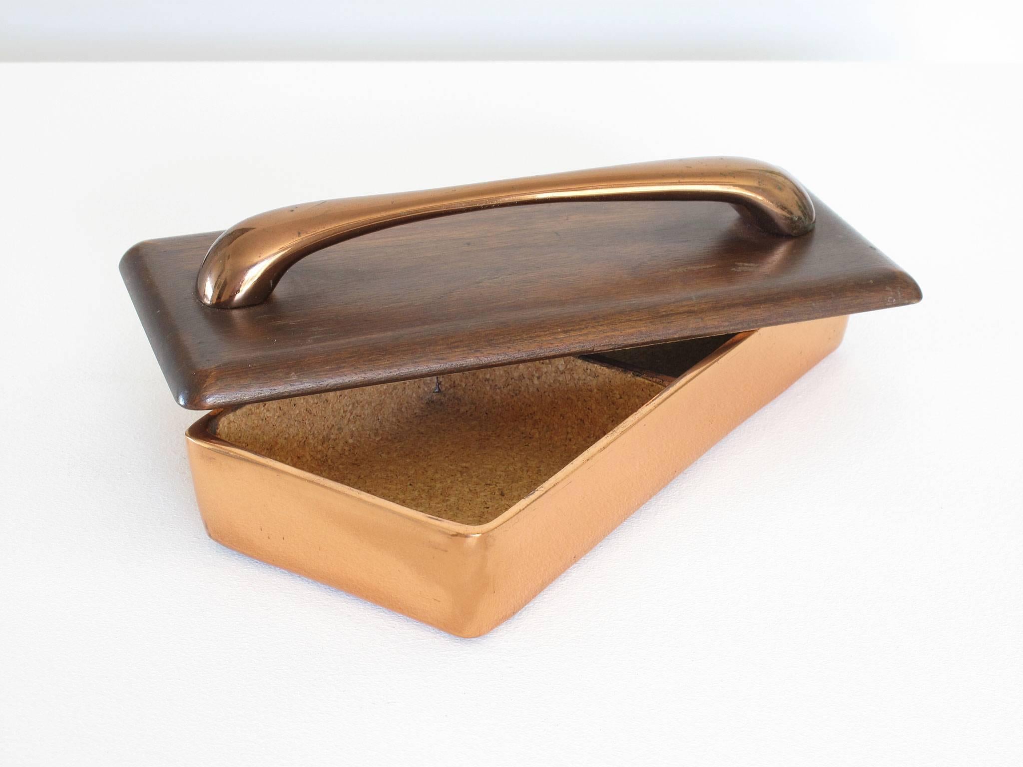 Ben Seibel
box, copper-plated metal, wood, cork and felt,
Jenfred Ware, New York, 1950s.

Copper-plated metal box, cork lined interior with two storage compartments, wood lid with copper handle, a handsome and versatile container for trinkets,