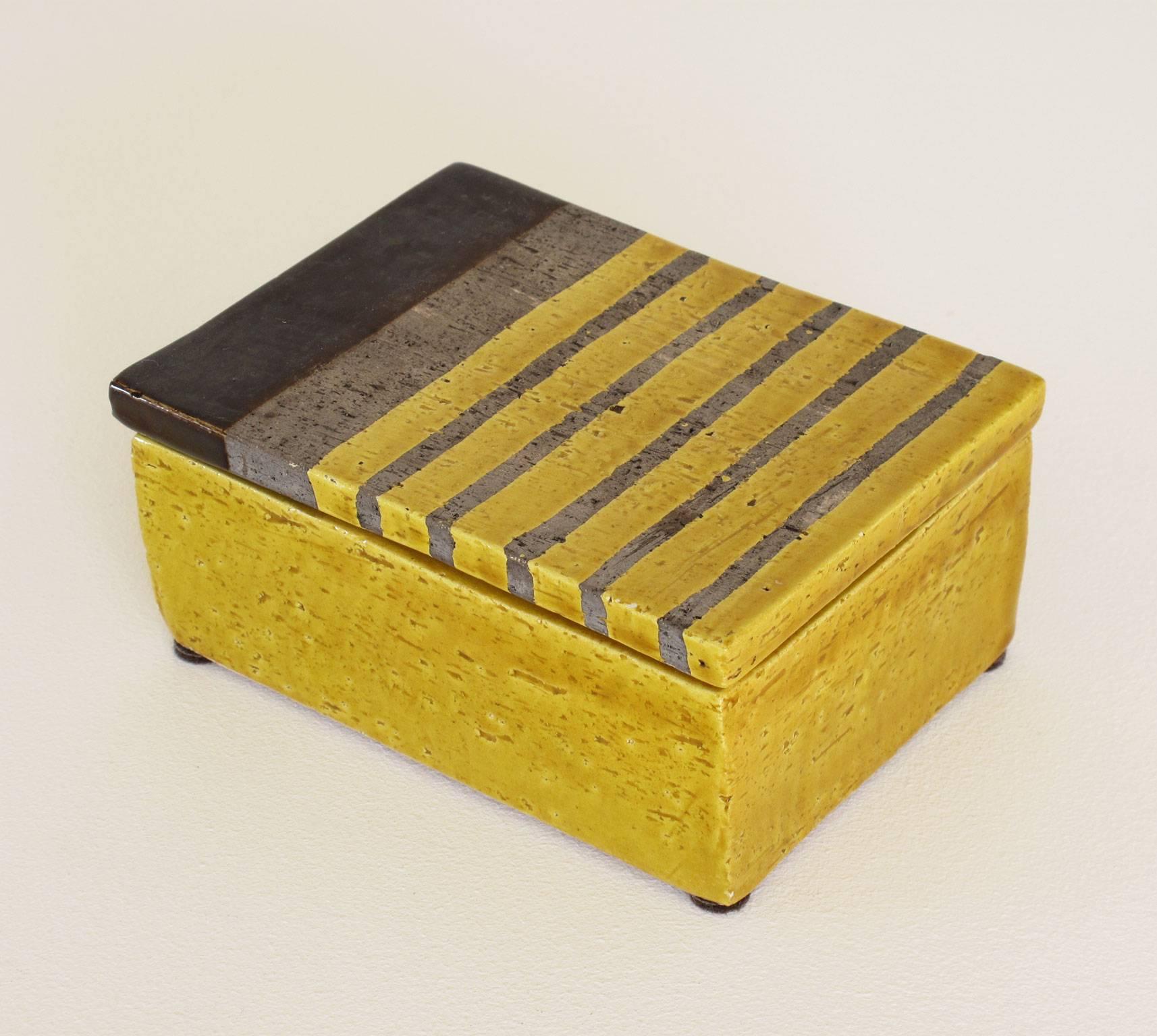 Handmade stoneware trinket stash box with brown and earth tones glazing, decorated with color blocking and striping over yellow, finished with a textured and glossy surface treatment, marked 'Italy' on bottom of box.

Dimensions: 2 1/4 high x 5