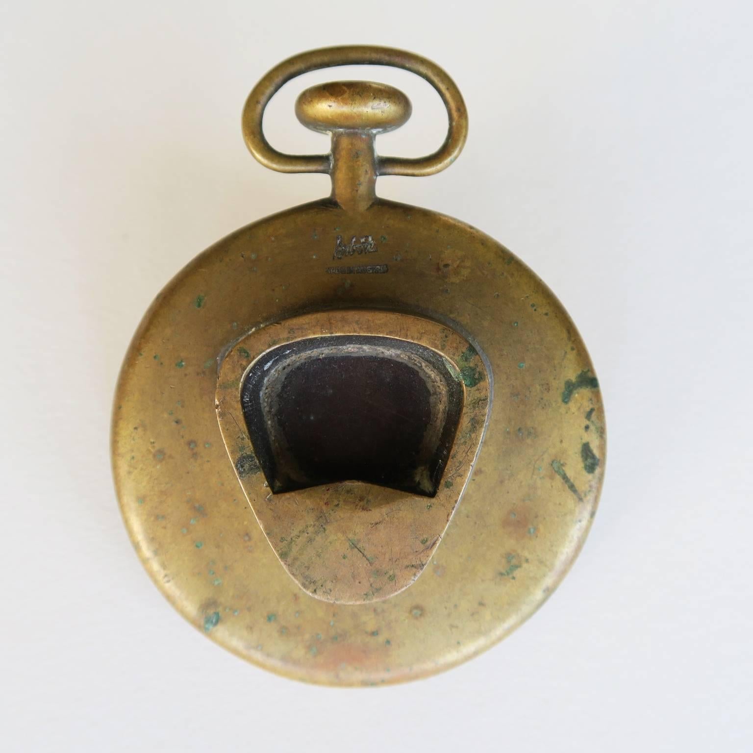 Carl Auböck designed solid brass object, heavy paperweight formed in the shape of an antique pocketwatch with bottle opener, 1950s, Werkstätte Auböck, Austria, signed with impressed mark, 3 1/2 x 2 1/2 x 5/8 inches.