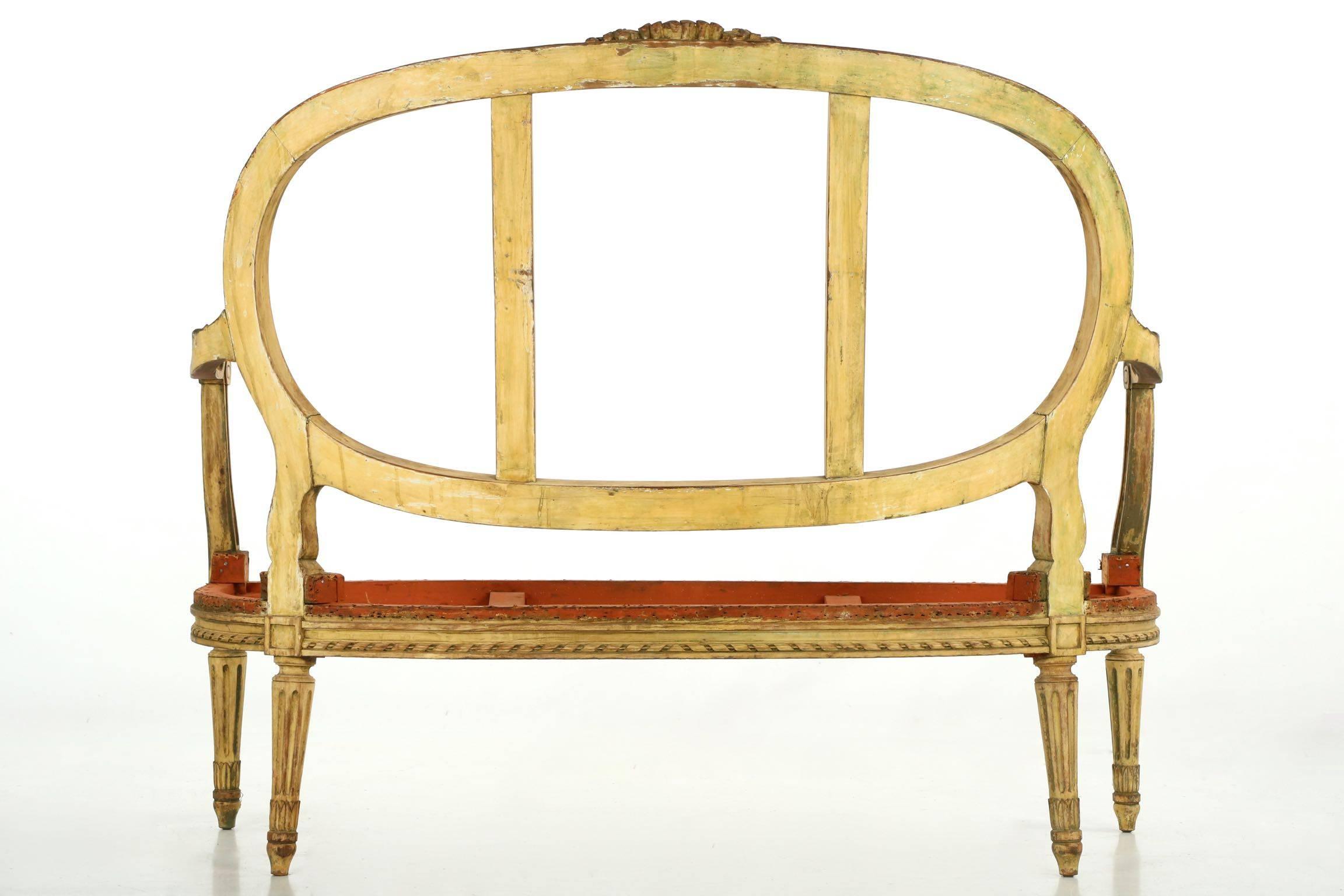 A naturally worn and distressed salon suite, the frames retain traces of original gilding with red bole peeking through the old off-white painted surfaces. Crisply carved and executed, the crest rail is an intricate display of florals over an